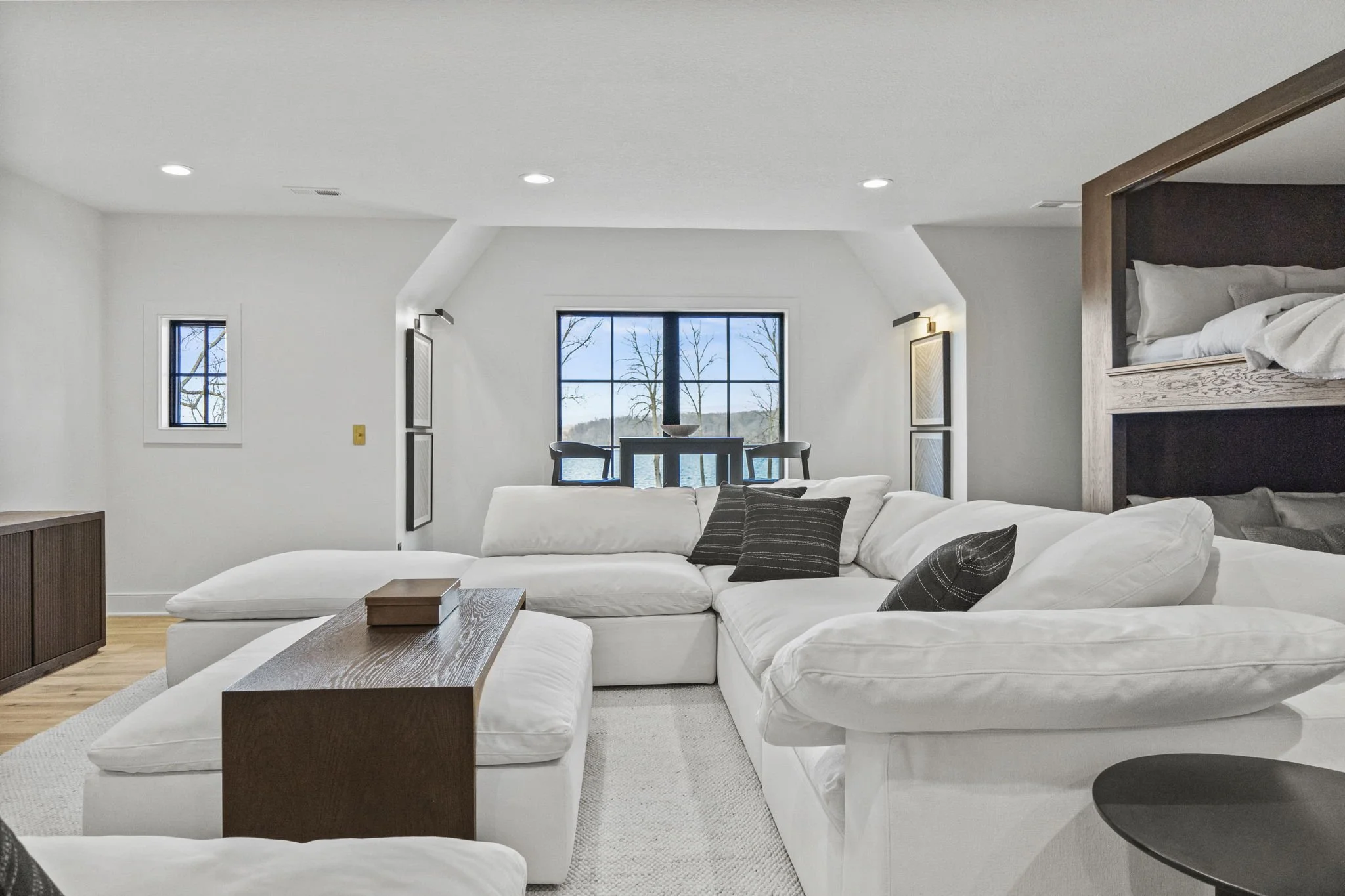 Bright living room with white sofa, wooden coffee table, and view of lake outside window