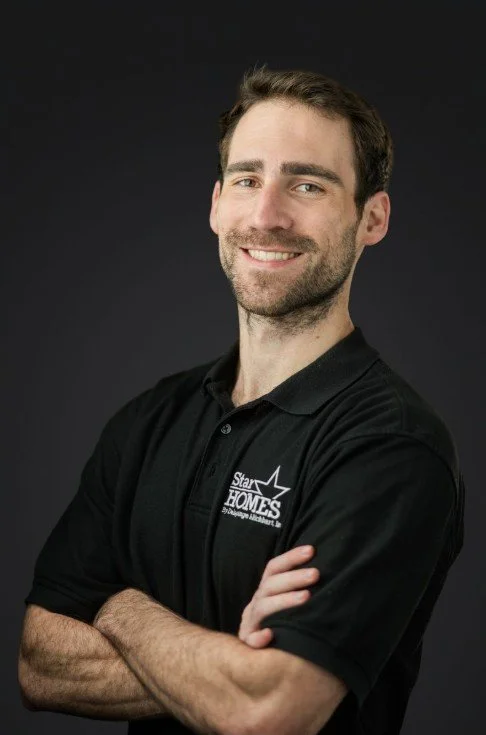 A smiling man with dark hair and a beard wearing a black polo shirt with a logo that says 'Star HOMES' against a dark background.