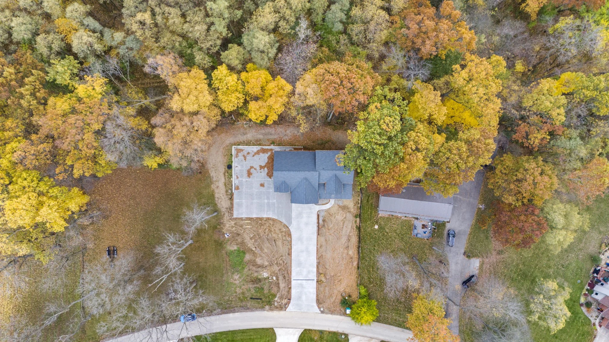 An aerial view of a house with a long driveway, surrounded by colorful fall trees with yellow, orange, and green leaves.