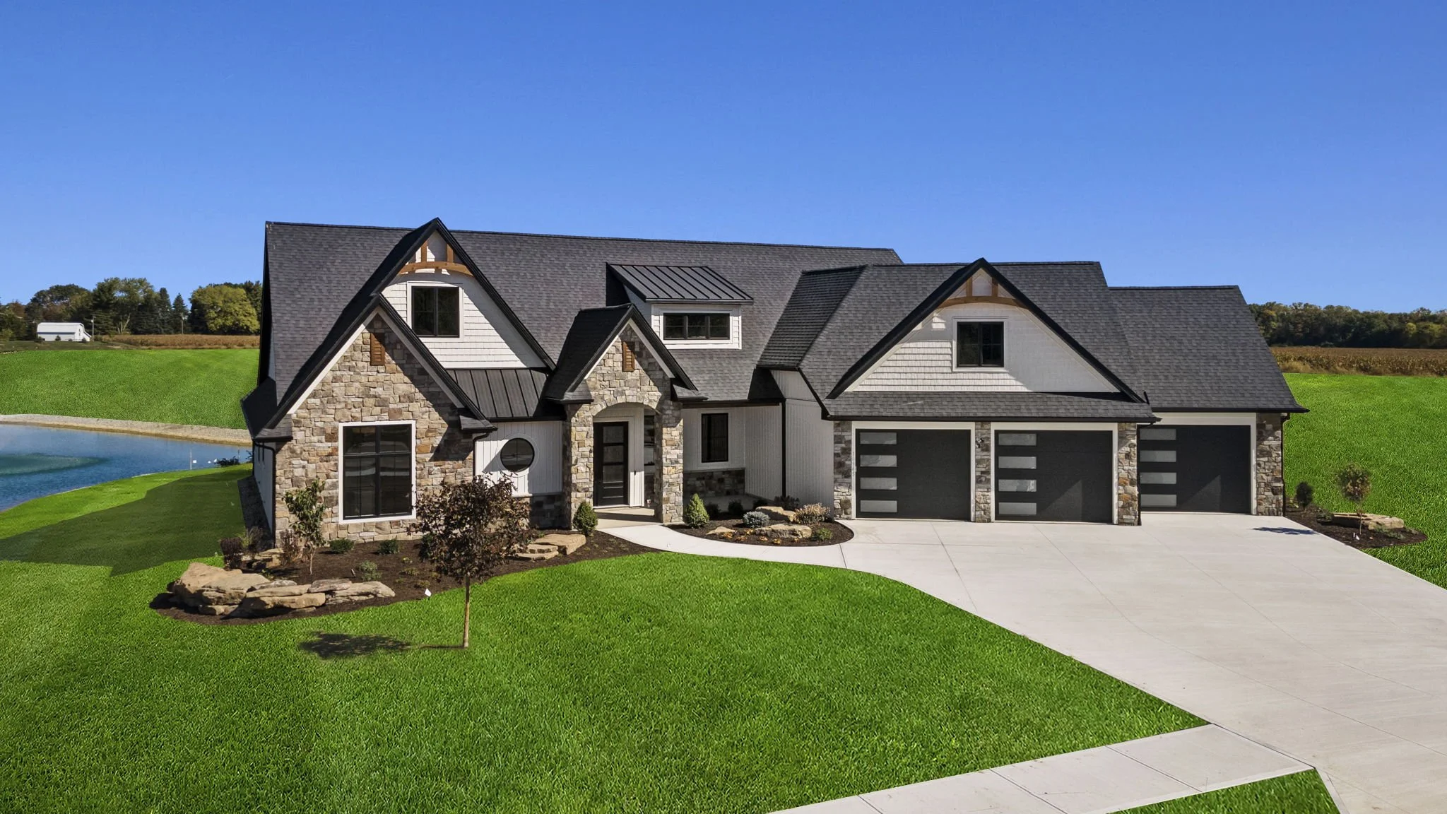 A large modern house with a stone and white exterior, dark roofing, and a three-car garage, surrounded by a manicured green lawn under a clear blue sky.