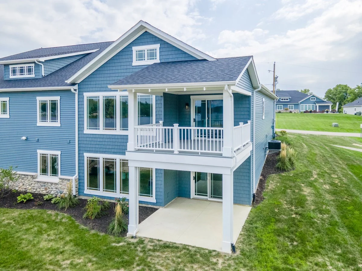 Rear view of a blue multi-story house with a balcony, sliding glass doors, and a lawn.