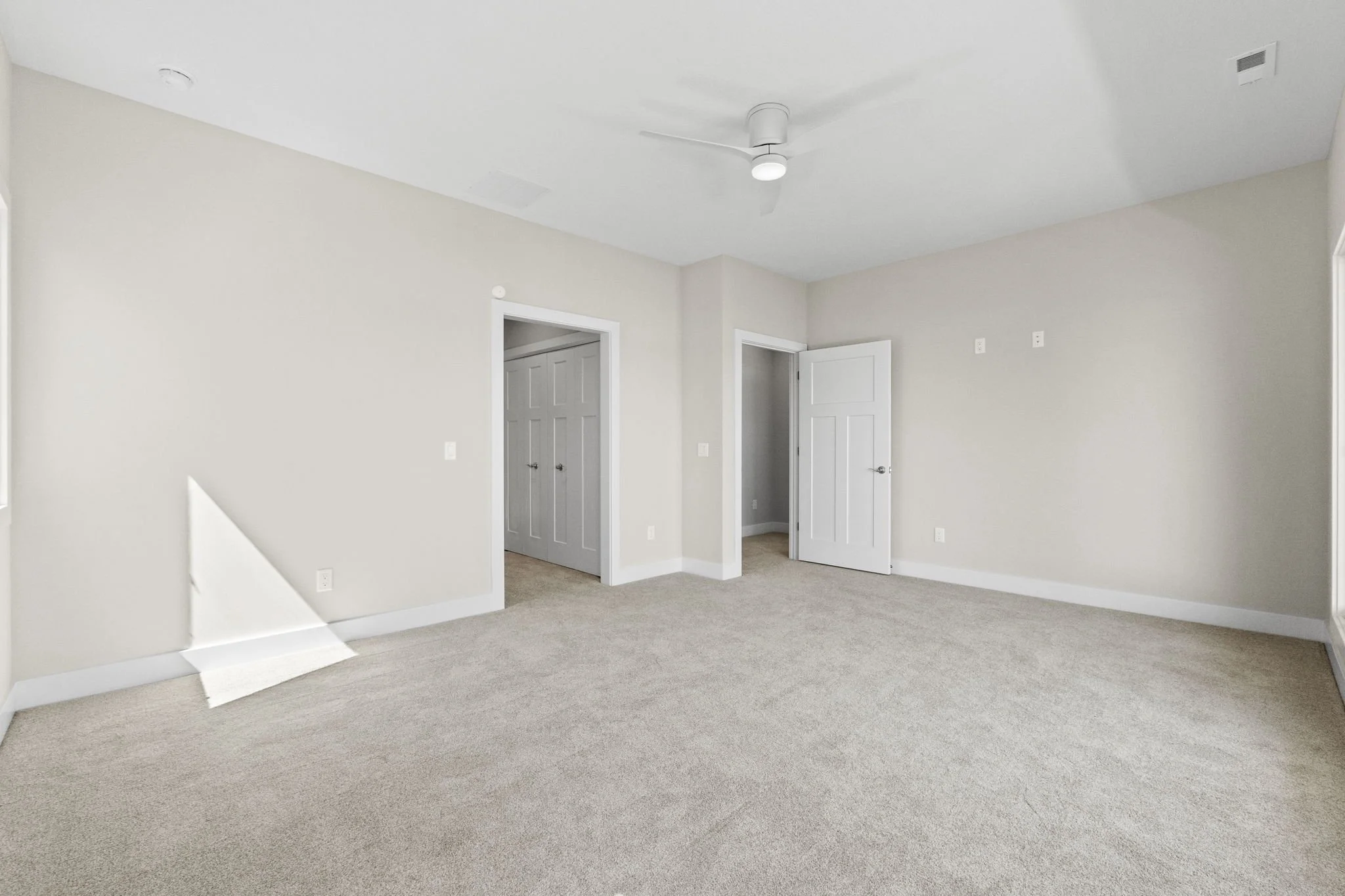 Empty room with beige walls and carpet, ceiling fan, and open closet doors.