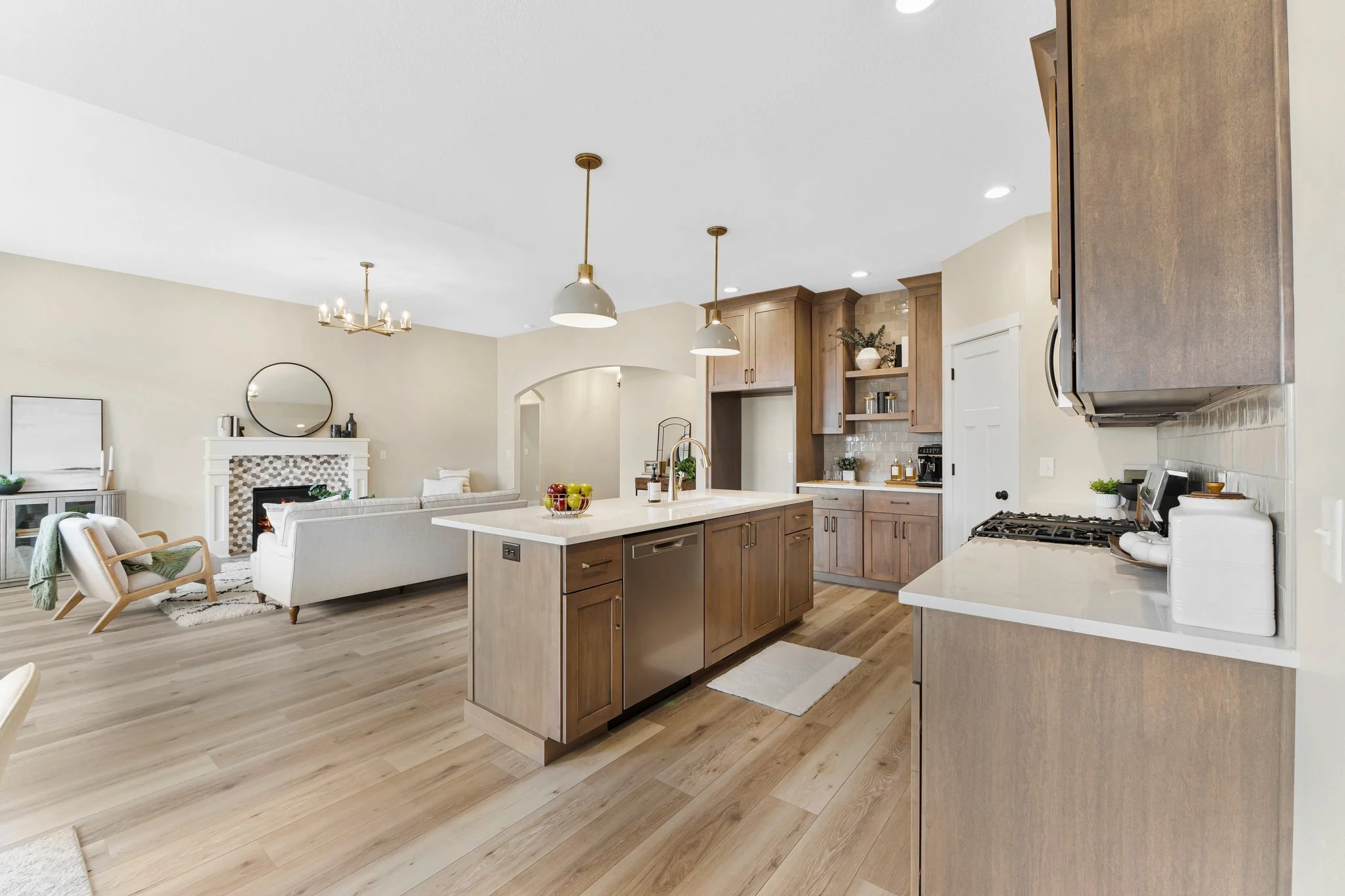Open-concept living room and kitchen with wooden cabinets, white countertops, pendant lights, and hardwood floors.