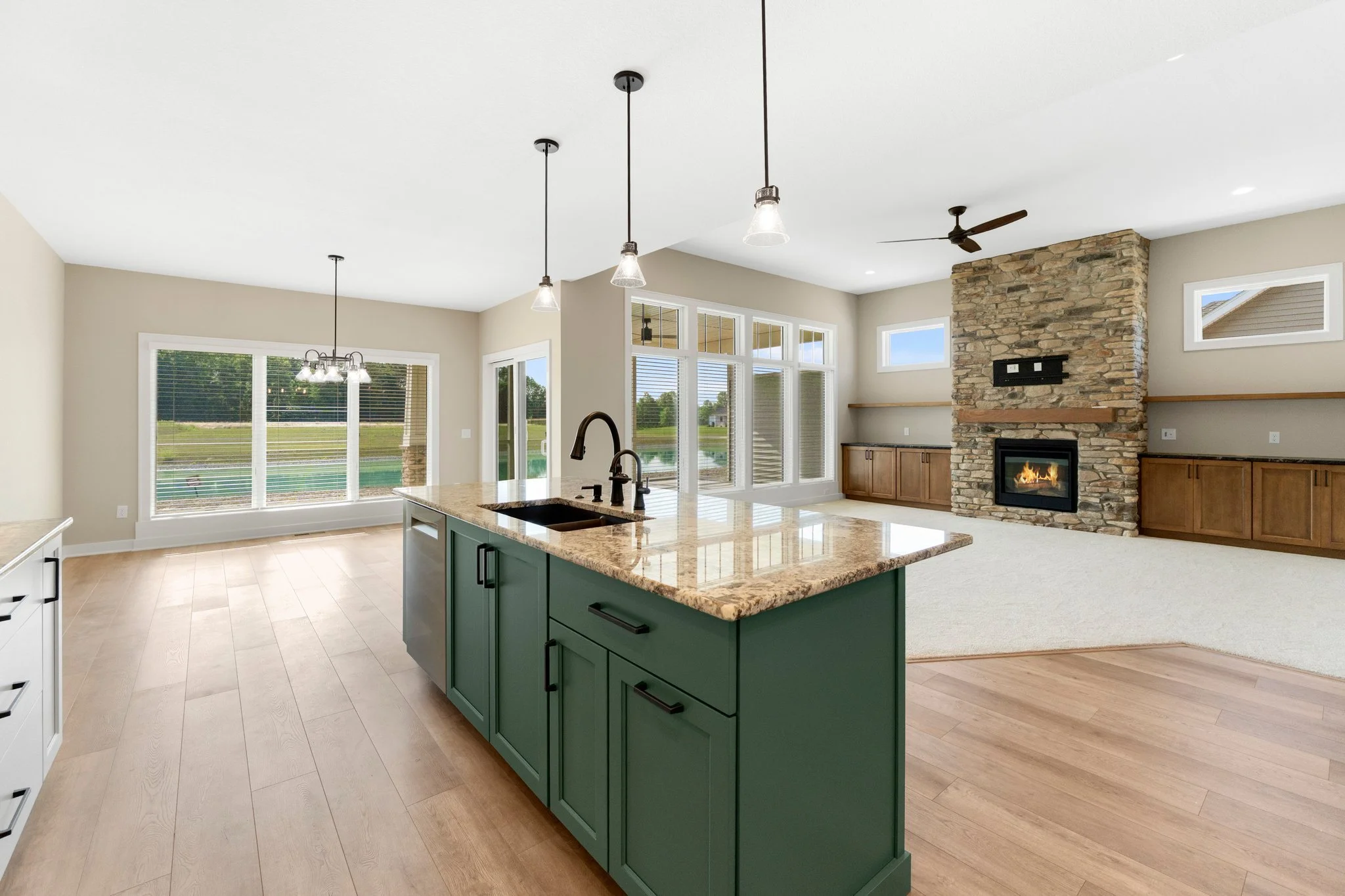 Open-concept living space with a kitchen island, large windows, and a stone fireplace.