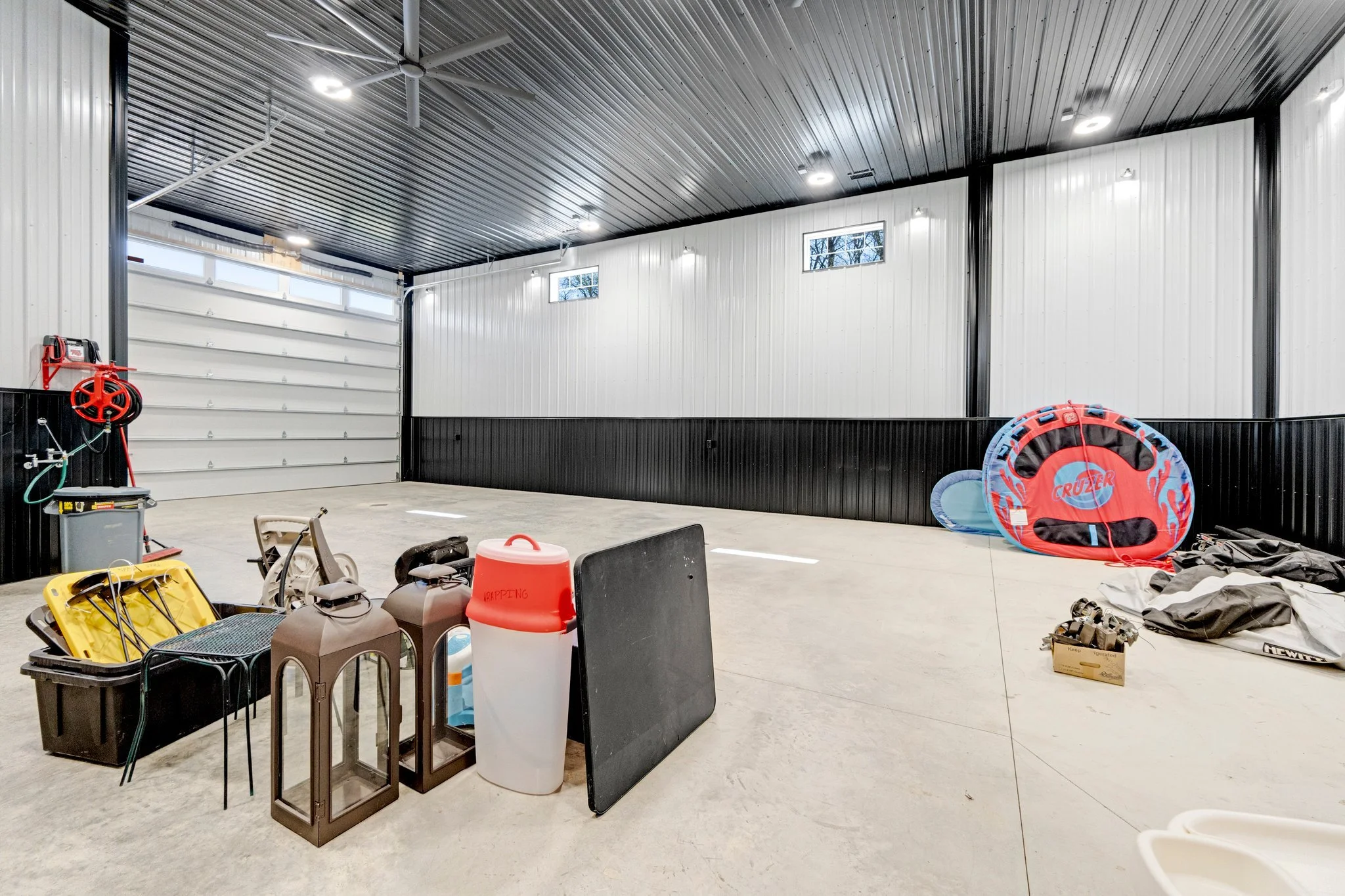 Empty garage with various outdoor equipment and supplies, including a red and blue inflatable pool, a fire hydrant, and storage boxes.