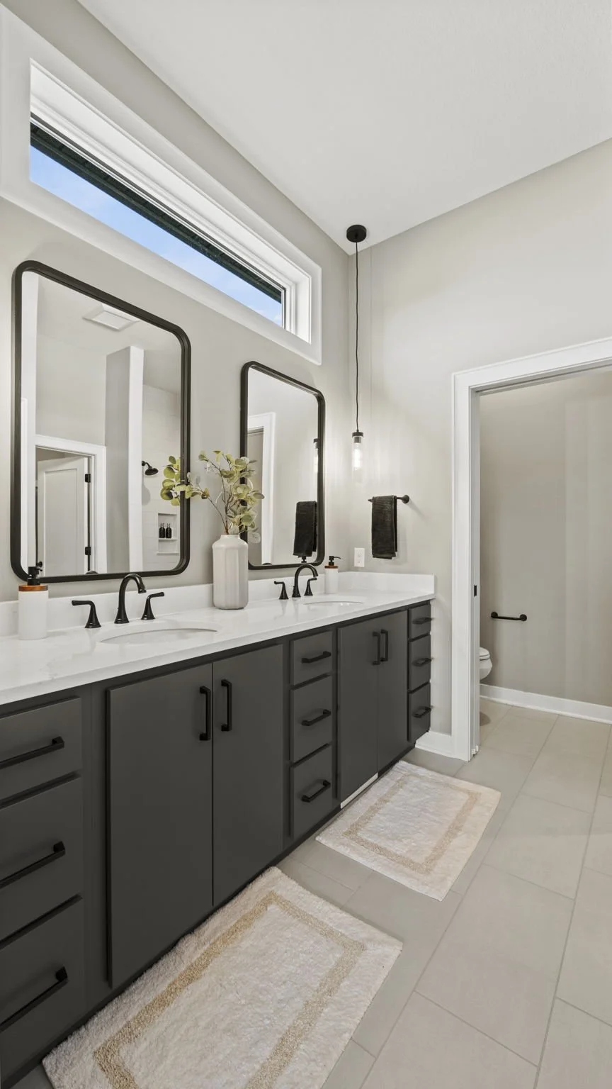 Modern bathroom with a double vanity, black fixtures, and a small window near the ceiling, featuring a twin sink setup, black framed mirrors, and neutral-toned decor.
