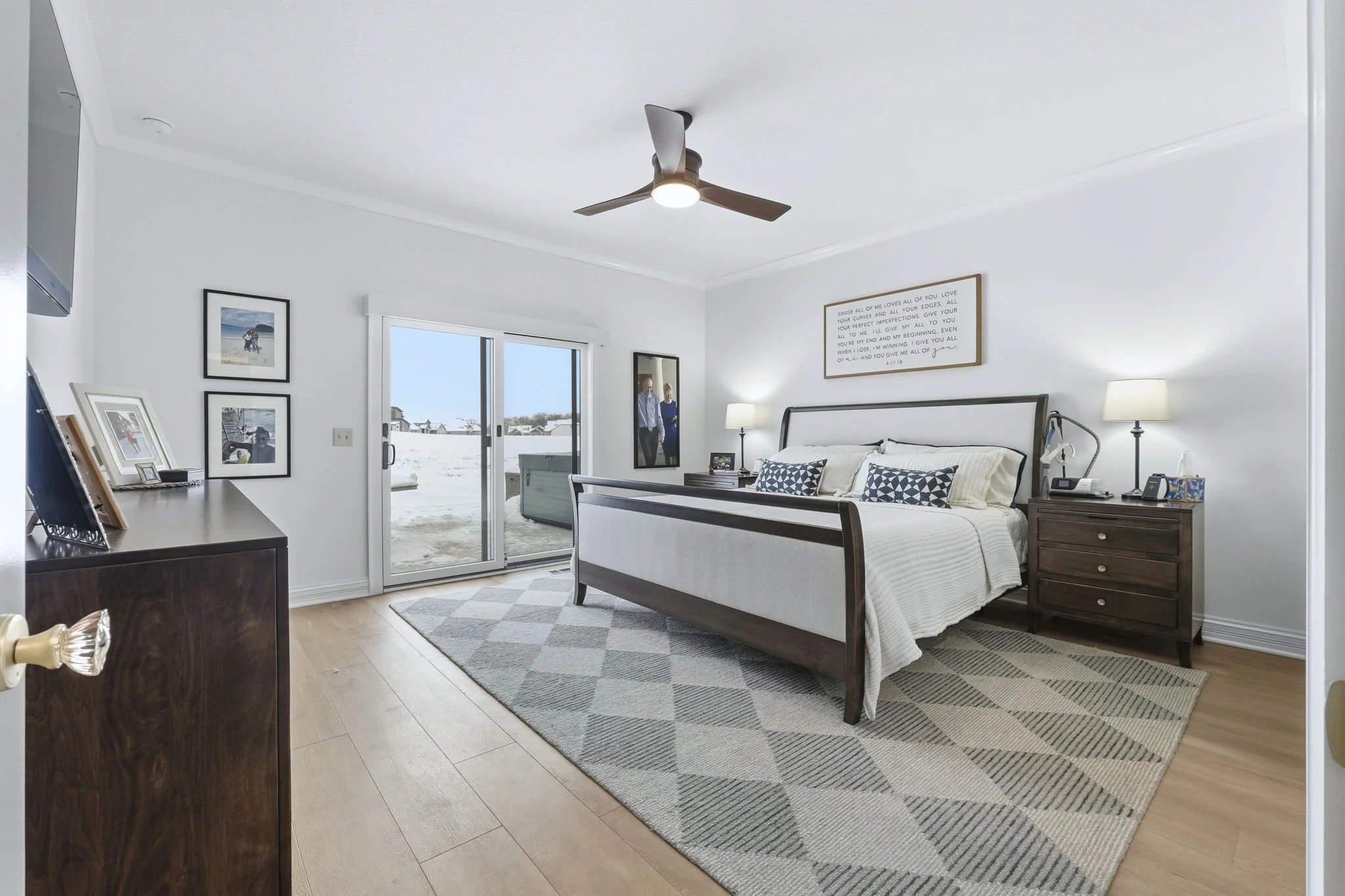 Bright bedroom with a bed, two nightstands with lamps, and a sliding glass door leading to a snowy balcony view.
