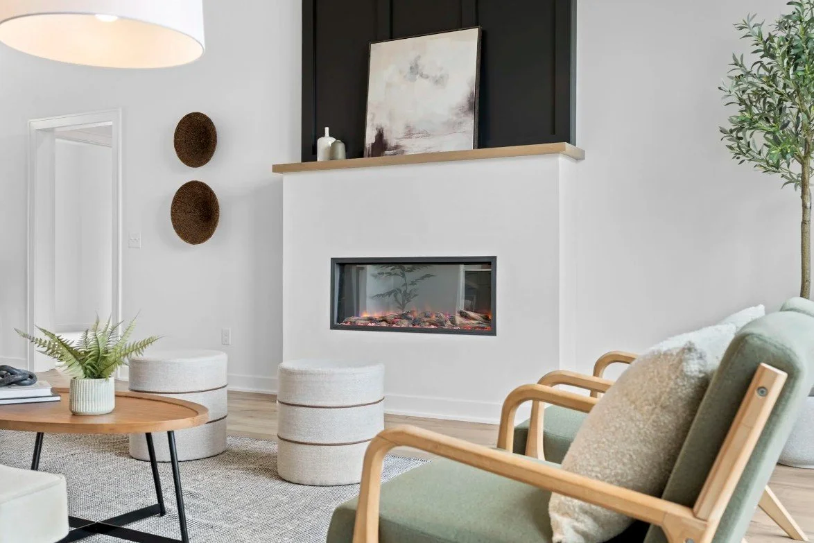Living room with modern fireplace, green armchairs, wooden coffee table, potted plant, and wall decor.