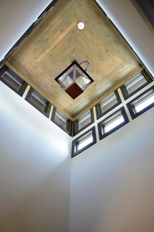 View of a ceiling with a knocked-out section of the roof showing windows around the edge and a hanging lantern in the center.