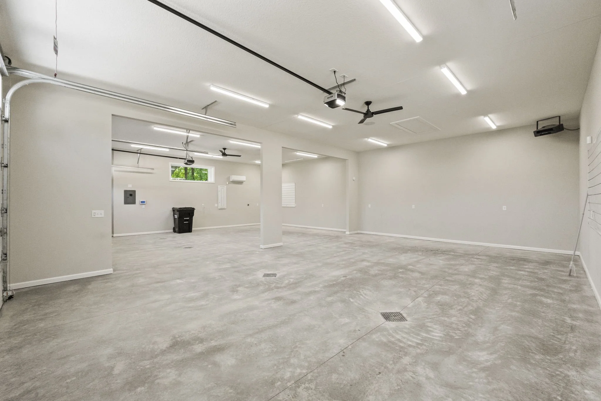 Empty garage converted into a clean, spacious room with concrete floor, white walls, ceiling fans, and fluorescent lighting.