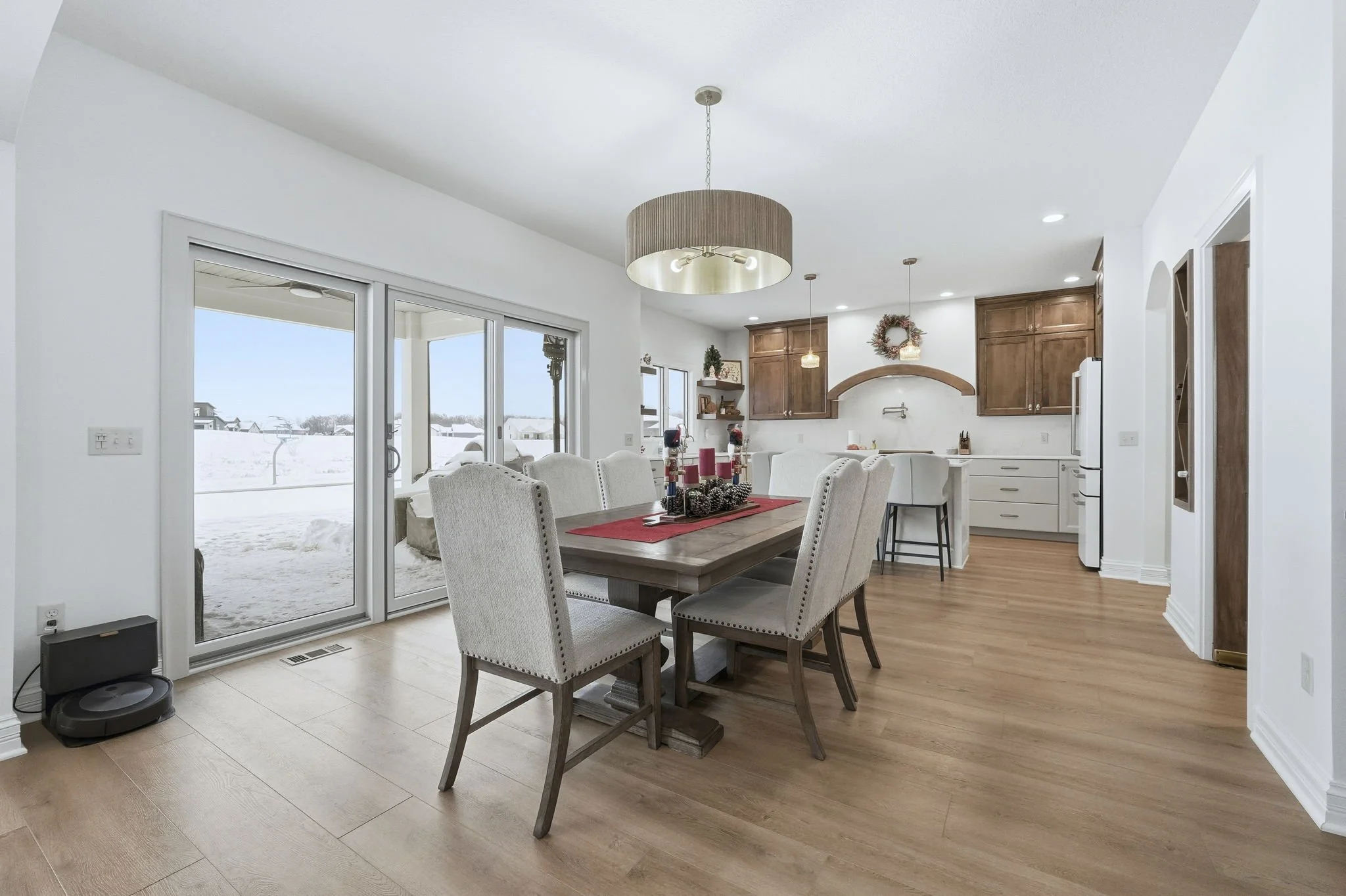 Dining room with a wooden table, beige upholstered chairs, holiday decorations, and a view of a snowy outdoor landscape through sliding glass doors.
