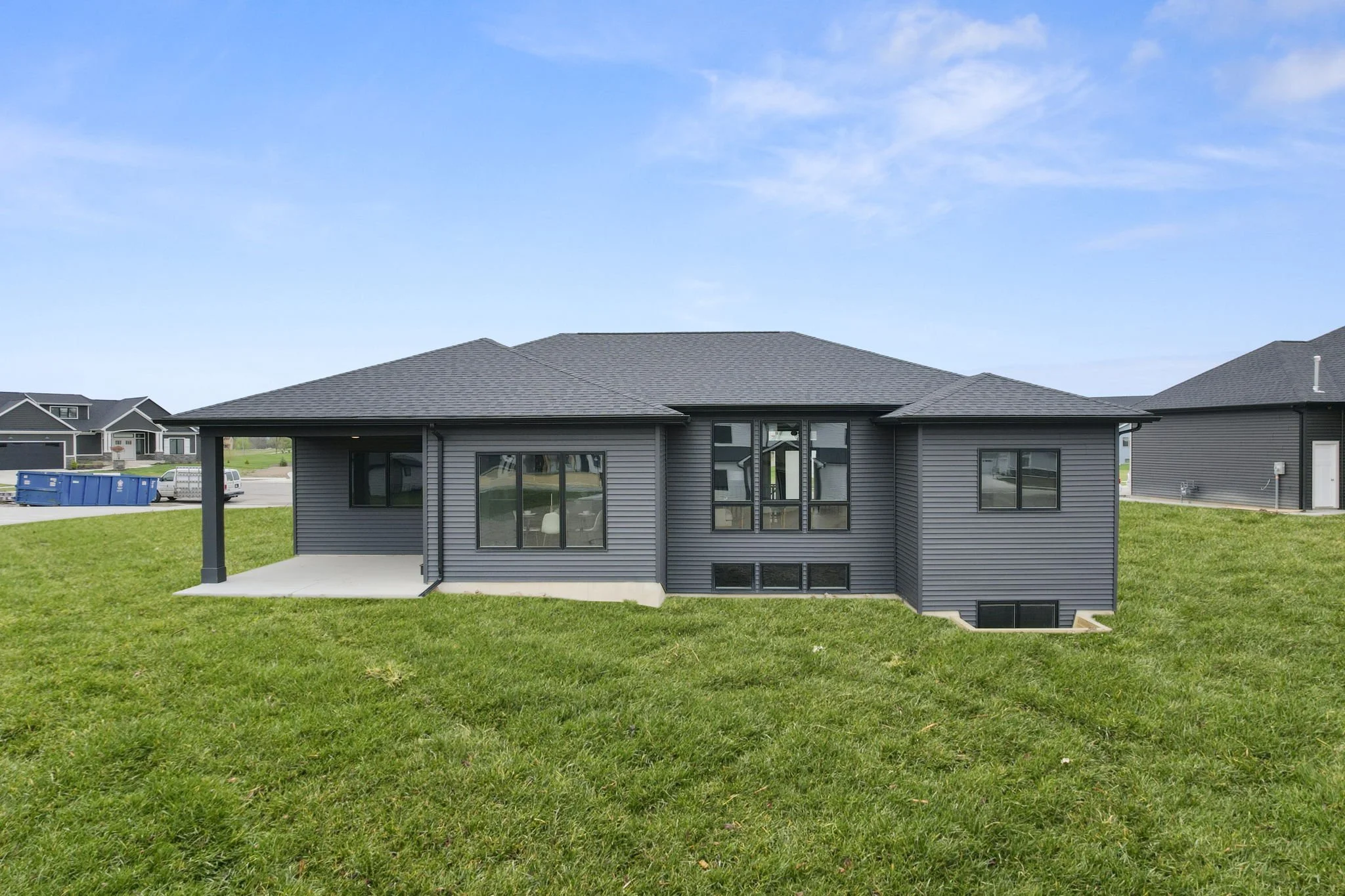 A modern gray house with large windows, situated on a green lawn with a clear blue sky overhead.