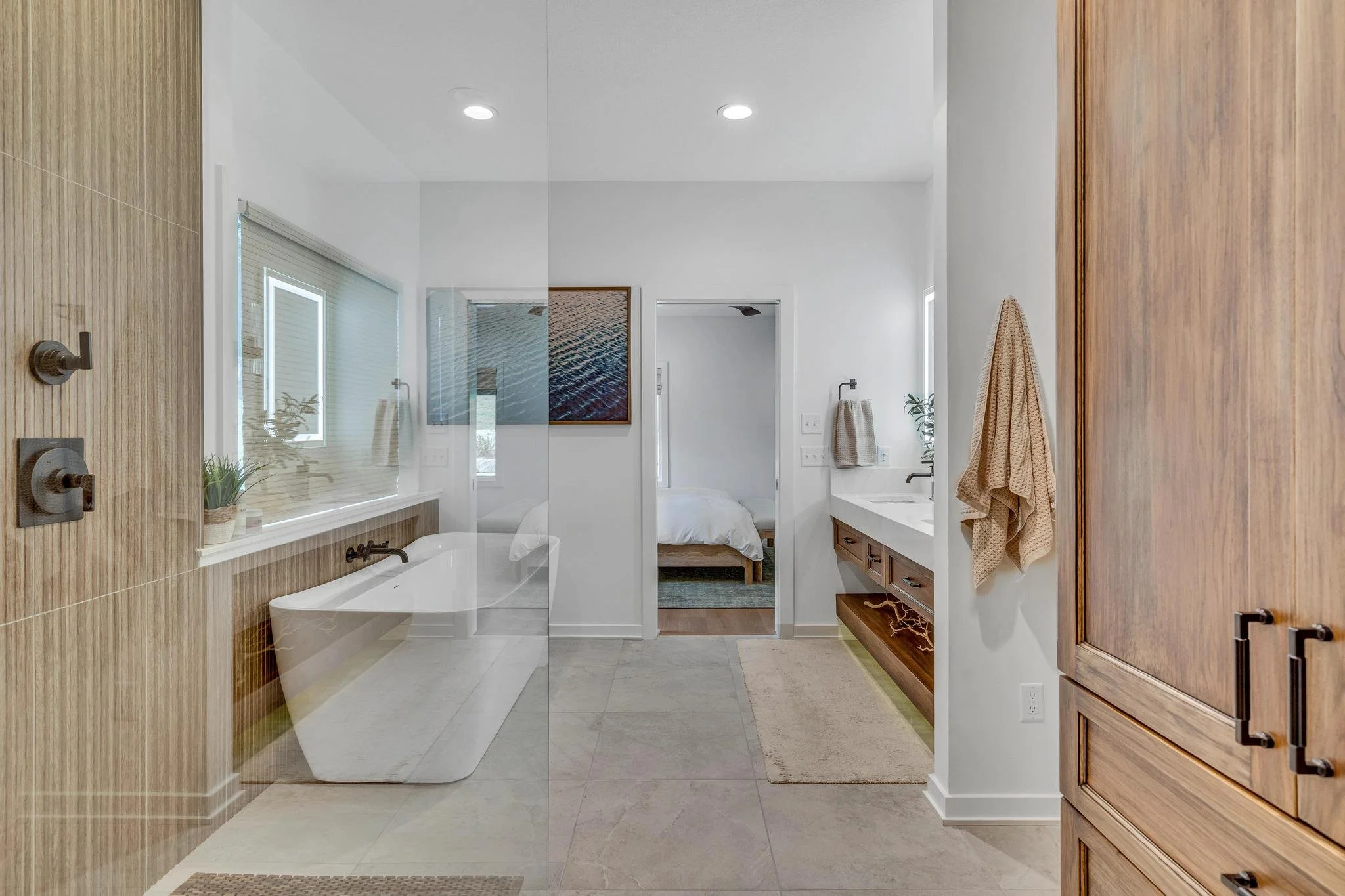 Modern bathroom with a bathtub, a walk-in shower with a glass partition, a vanity with a sink, and a separate bedroom visible through an open doorway.