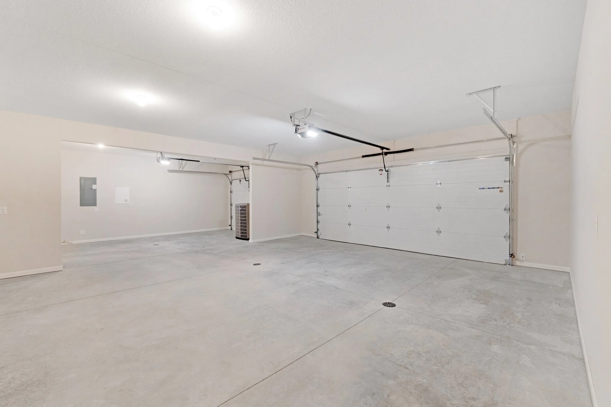 Empty two-car garage with white walls, concrete floor, and closed white garage doors.