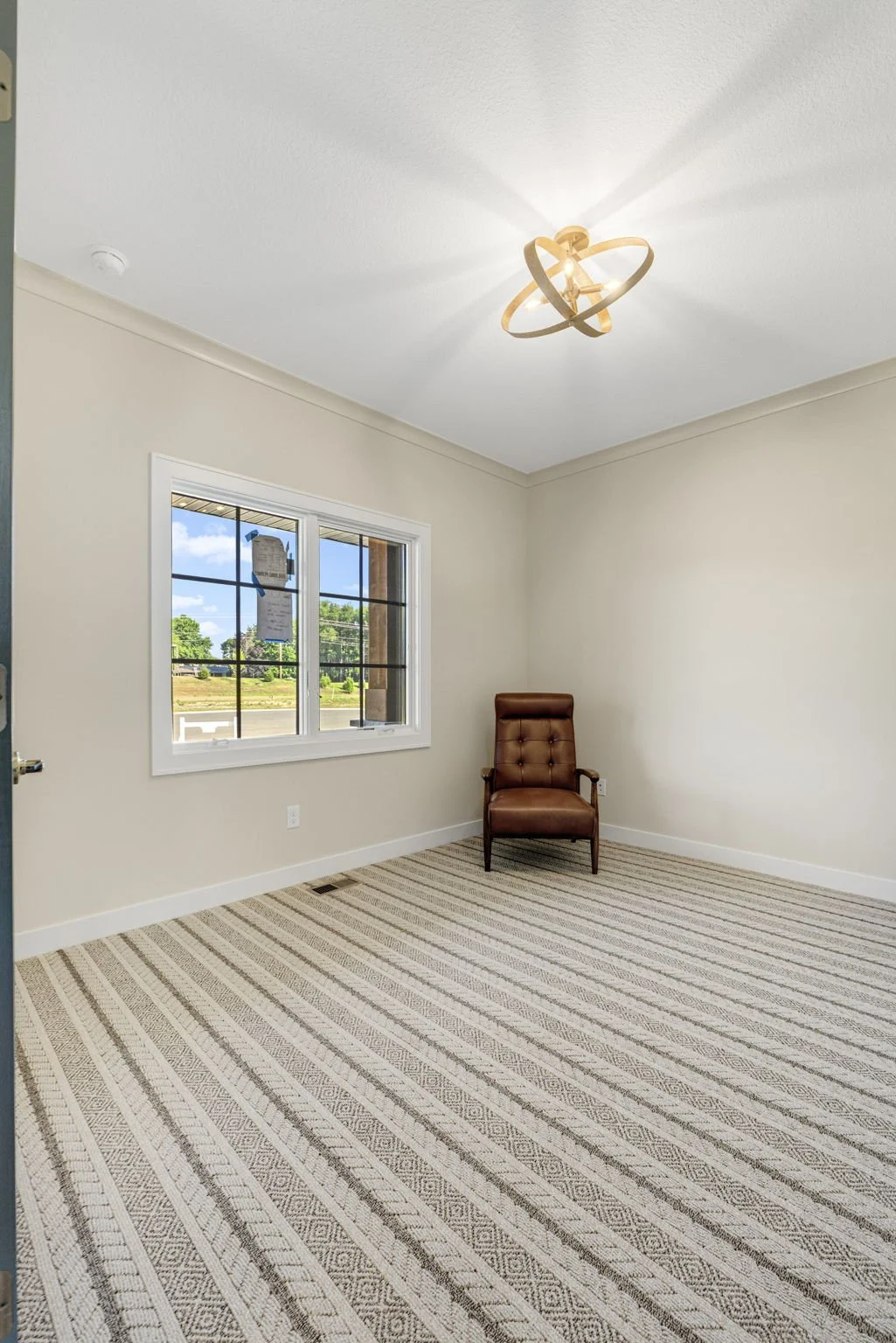 Empty room with a brown armchair, window, and modern ceiling light fixture.