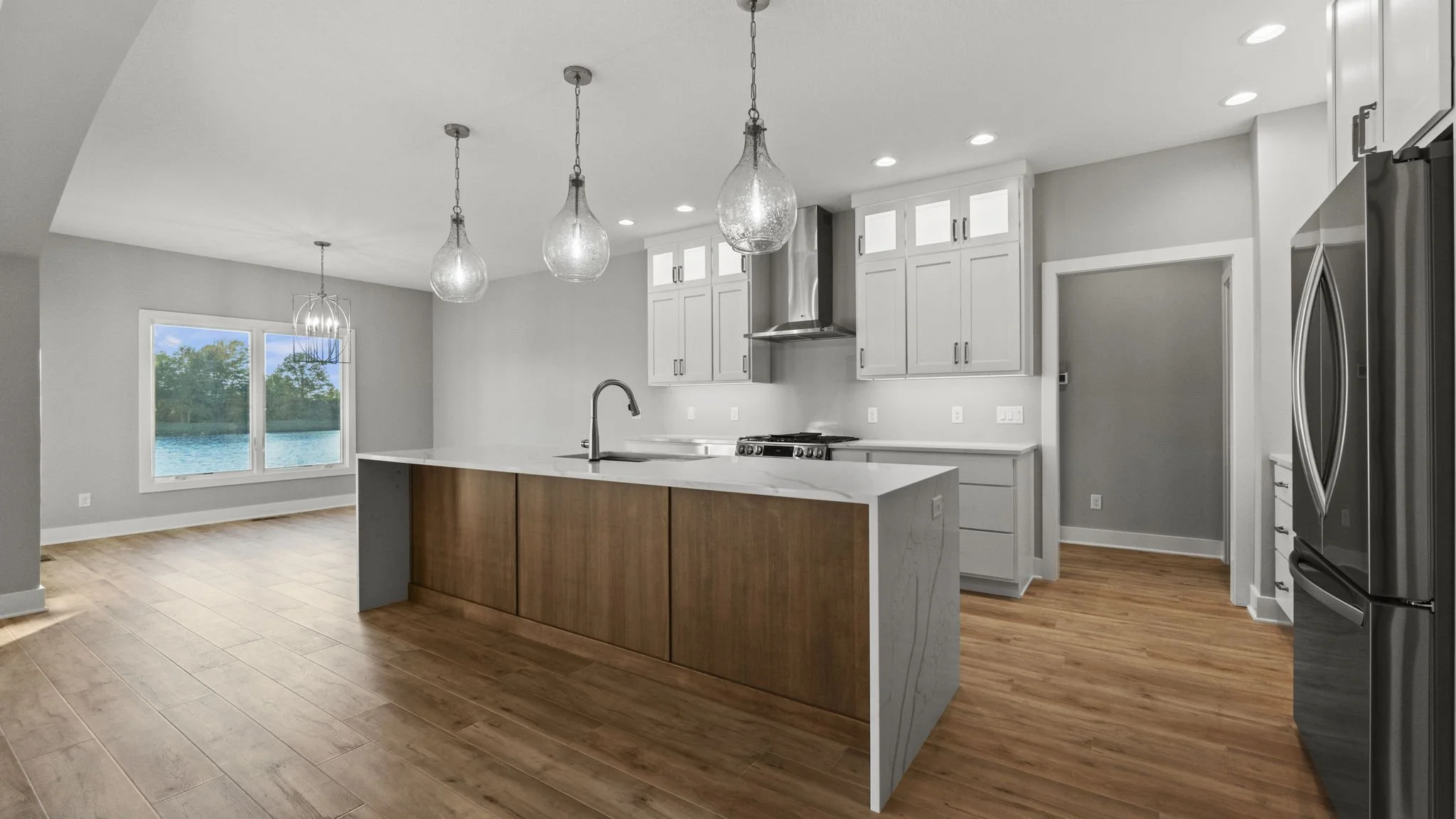 Modern kitchen with wooden island, white cabinets, stainless steel appliances, pendant lights, and hardwood floor overlooking a waterfront view.