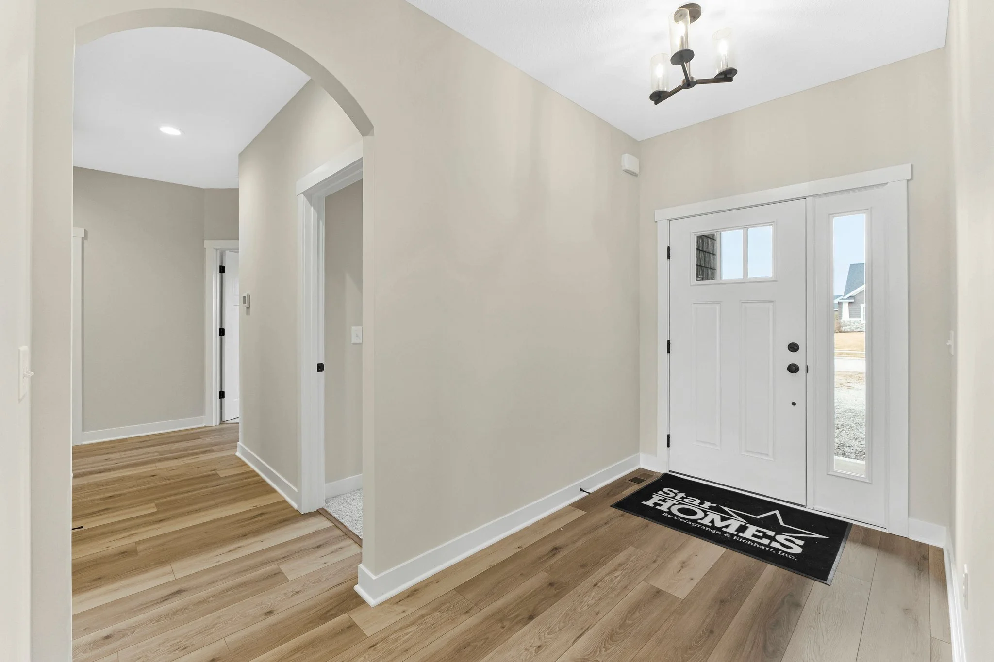 An entryway with a white door and windows, a black welcome mat, light wood flooring, and beige walls.