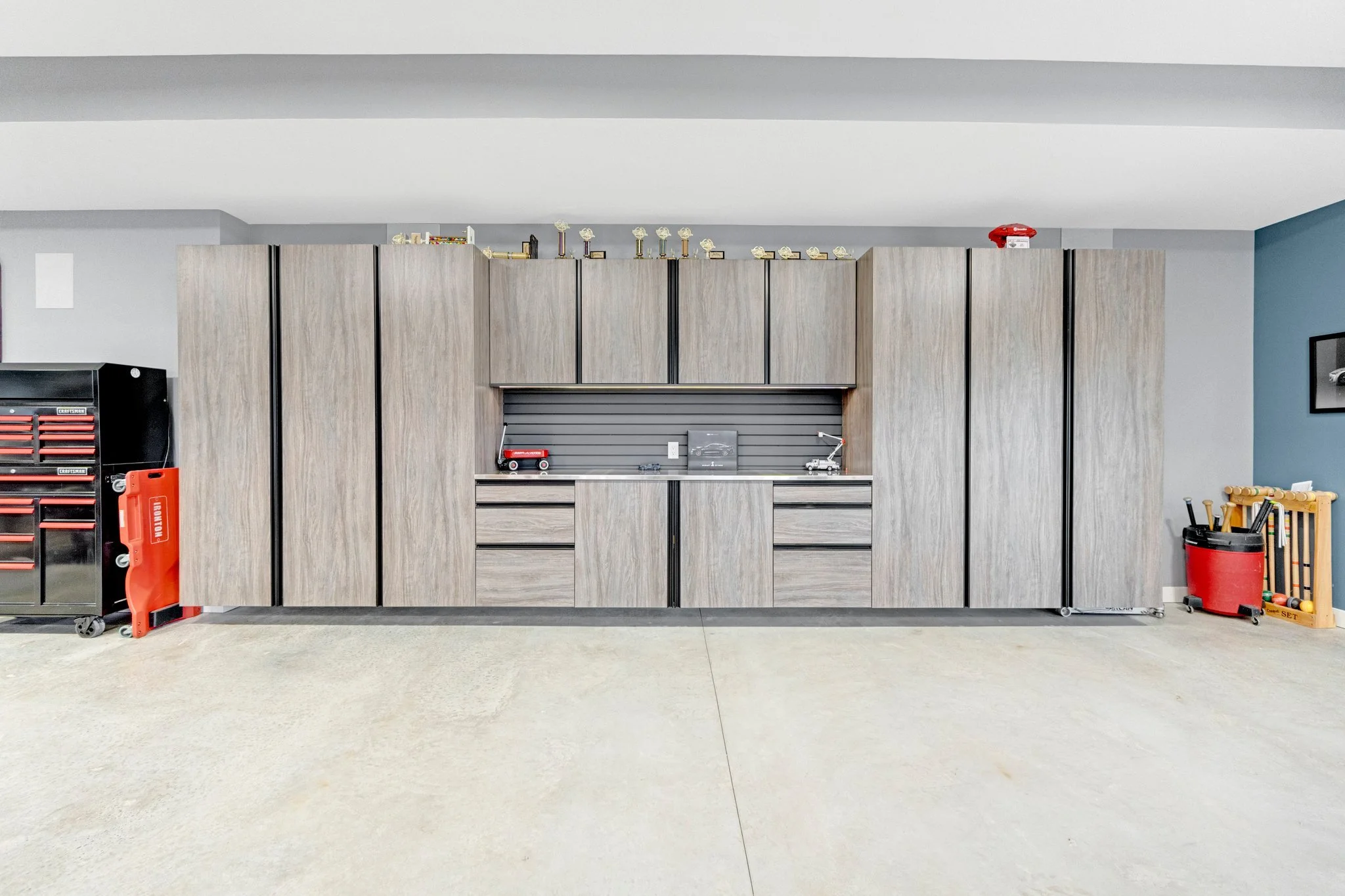 A large wooden storage cabinet with multiple doors and drawers in a garage setting, with tools and equipment on the sides and top.