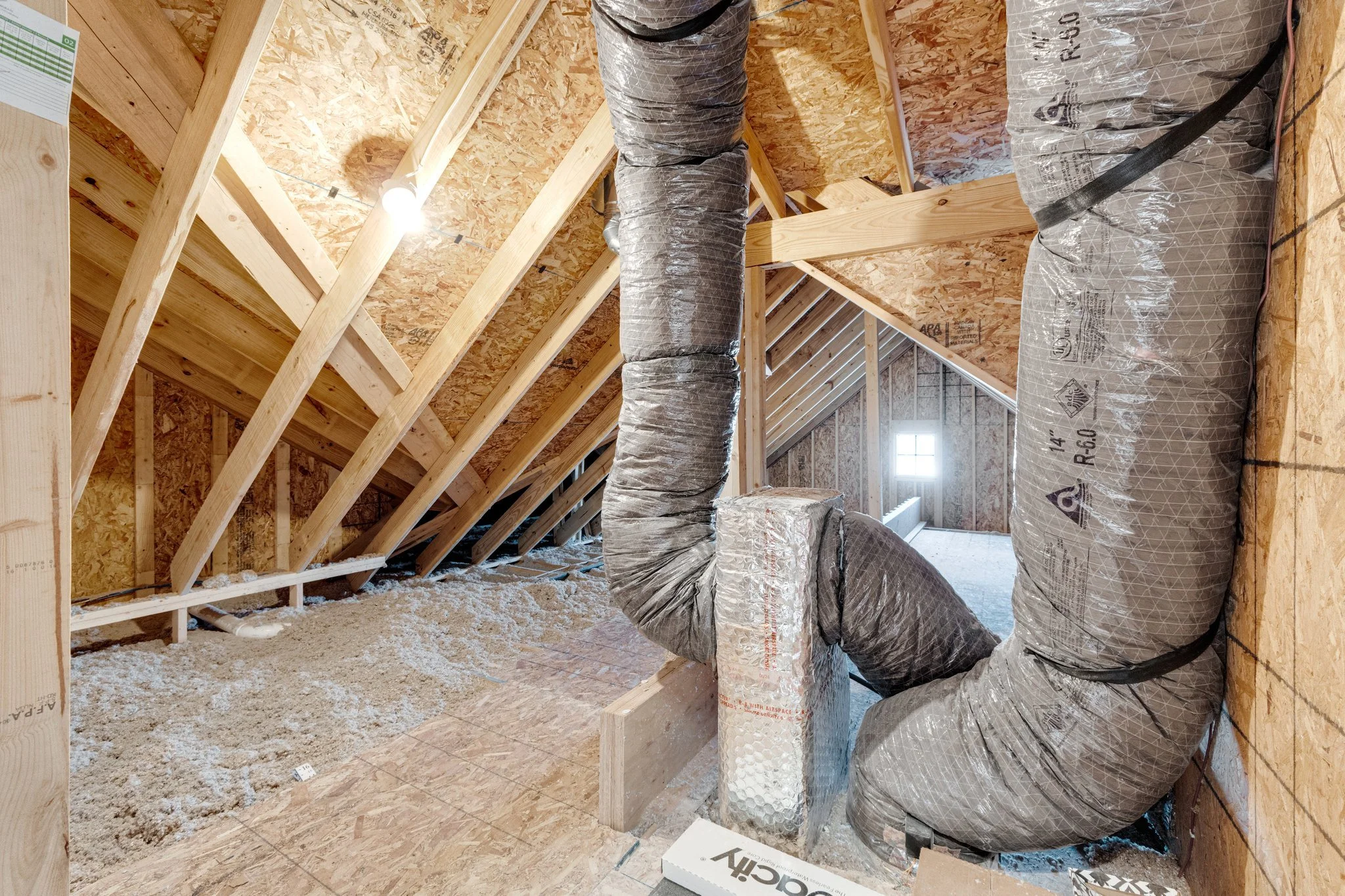 Attic under construction showing wooden framing, insulation, and ductwork.