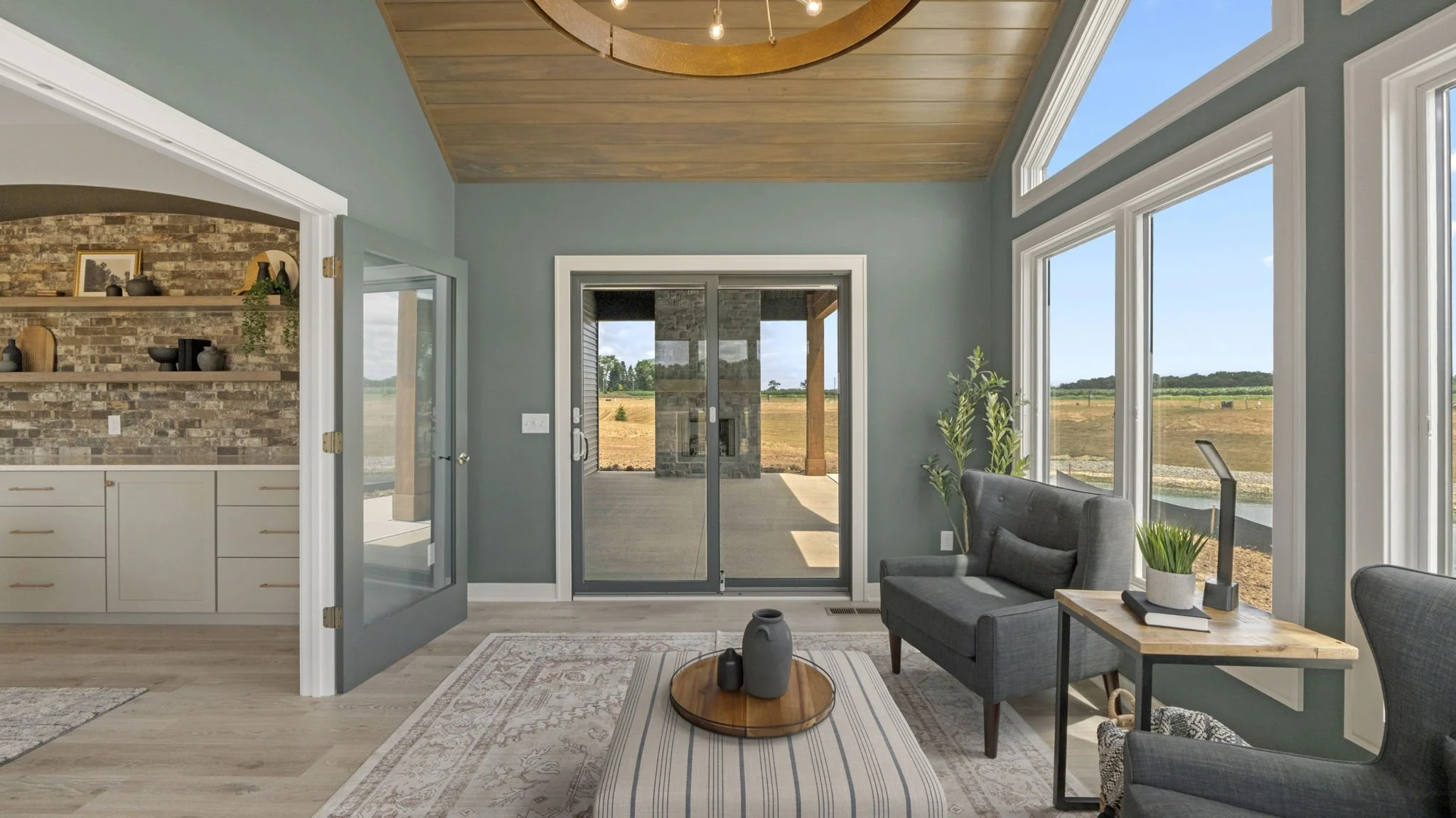 Living room with large windows, green walls, wooden ceiling, glass sliding door to porch, gray furniture, and view of outdoor landscape