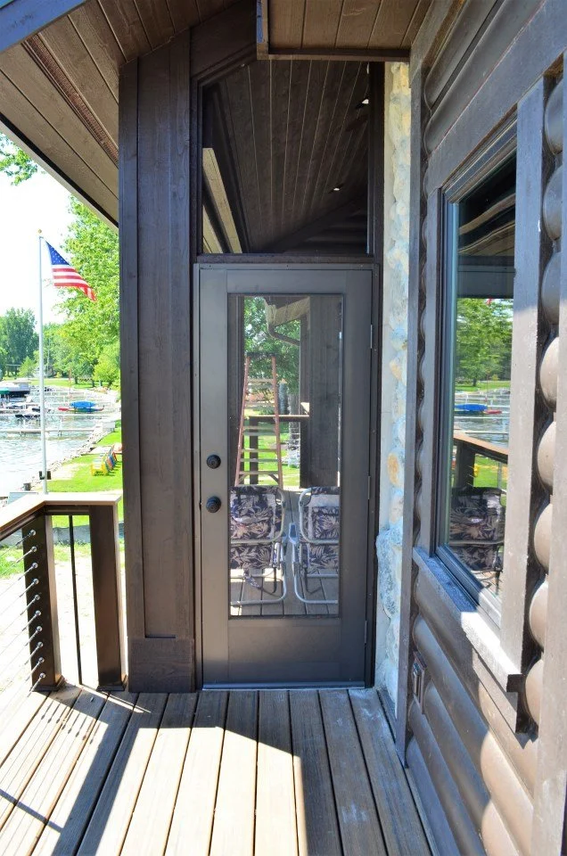 View of a porch with a glass door, chairs outside, and a boat marina with the American flag flying in the background.