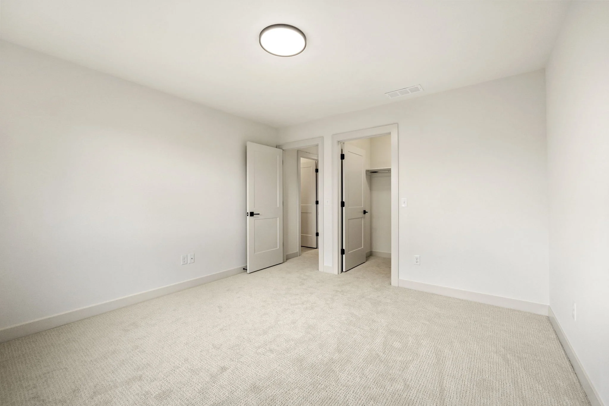 Empty bedroom with white walls, beige carpet, and open closet doors.