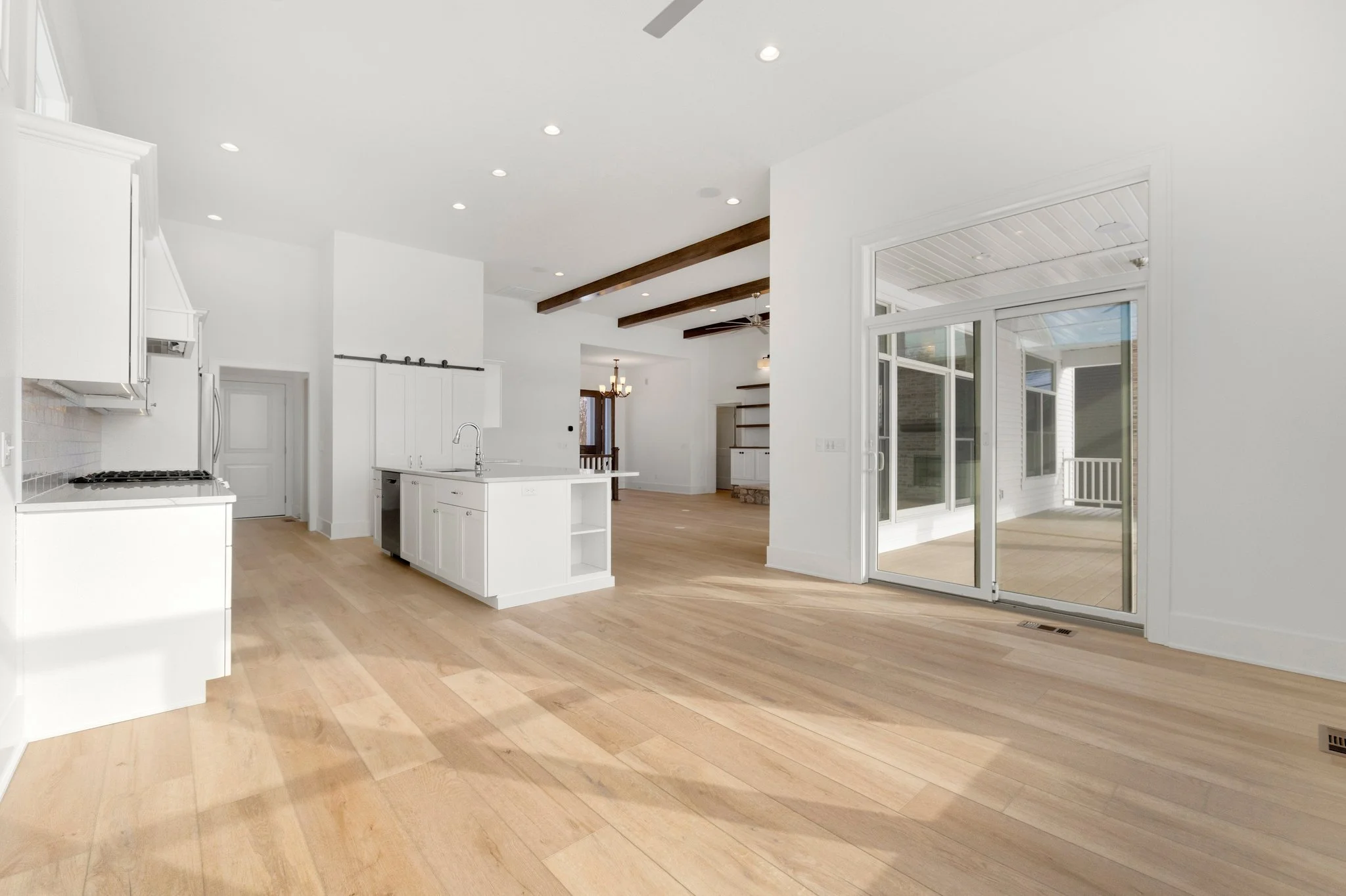 Empty modern open-concept kitchen and living area with white cabinets, hardwood flooring, and large sliding glass doors leading to a patio.