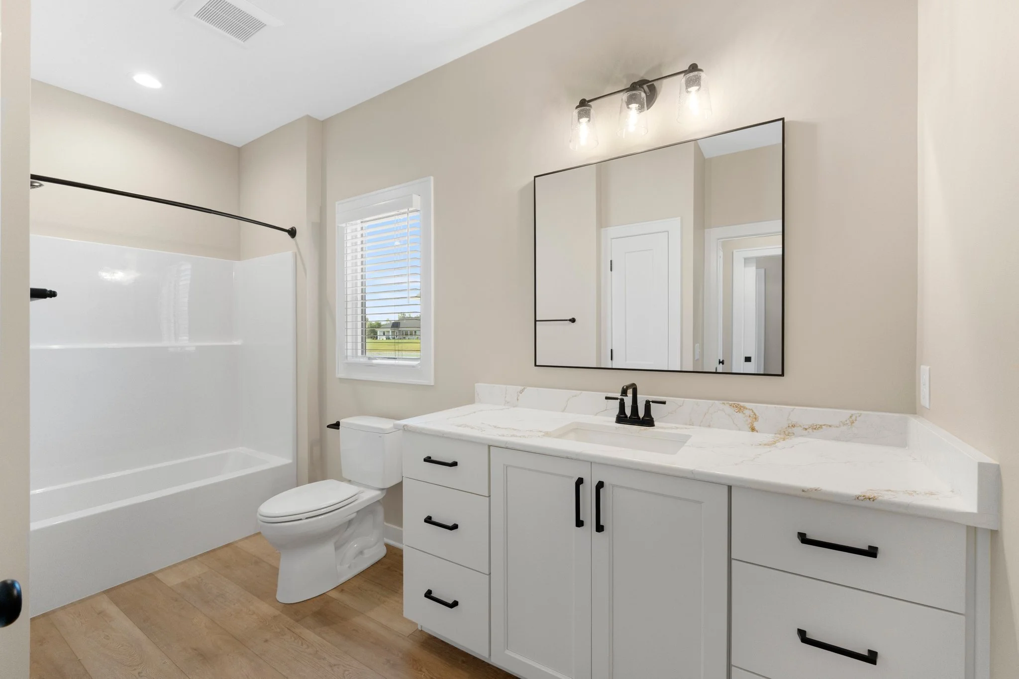 Modern bathroom with a white vanity, marble countertop, black fixtures, mirror, window with blinds, and a bathtub with black curtain rod.