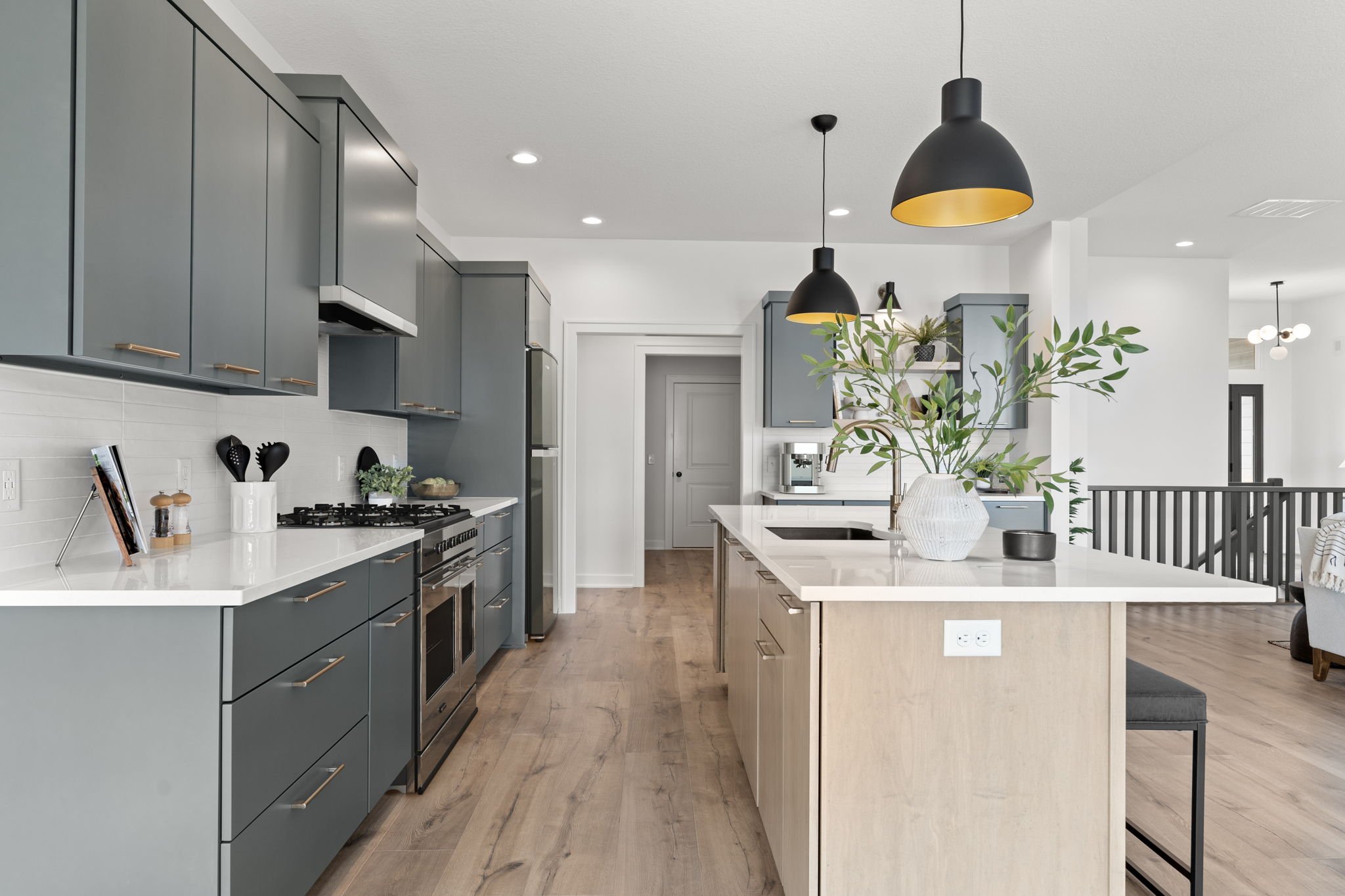 Modern kitchen with blue cabinets, a white island with a large plant in a vase, black pendant lights, and hardwood floors.