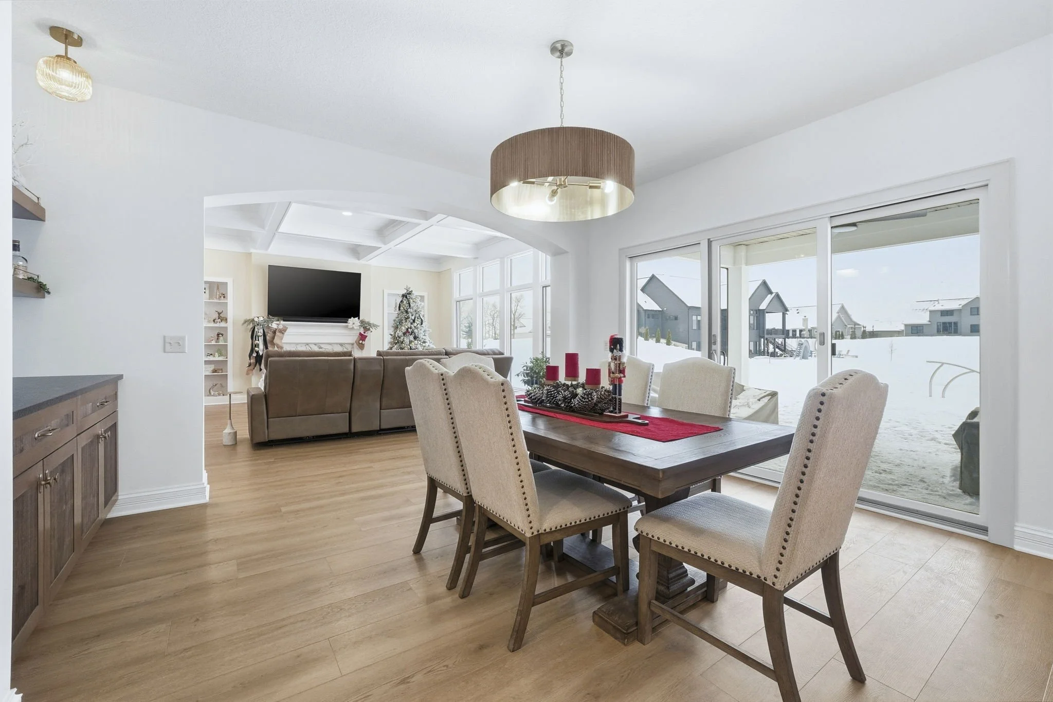 Living room and dining area with large windows and sliding doors showing snow outside, decorated for Christmas with a Christmas tree, stockings, and holiday candles.