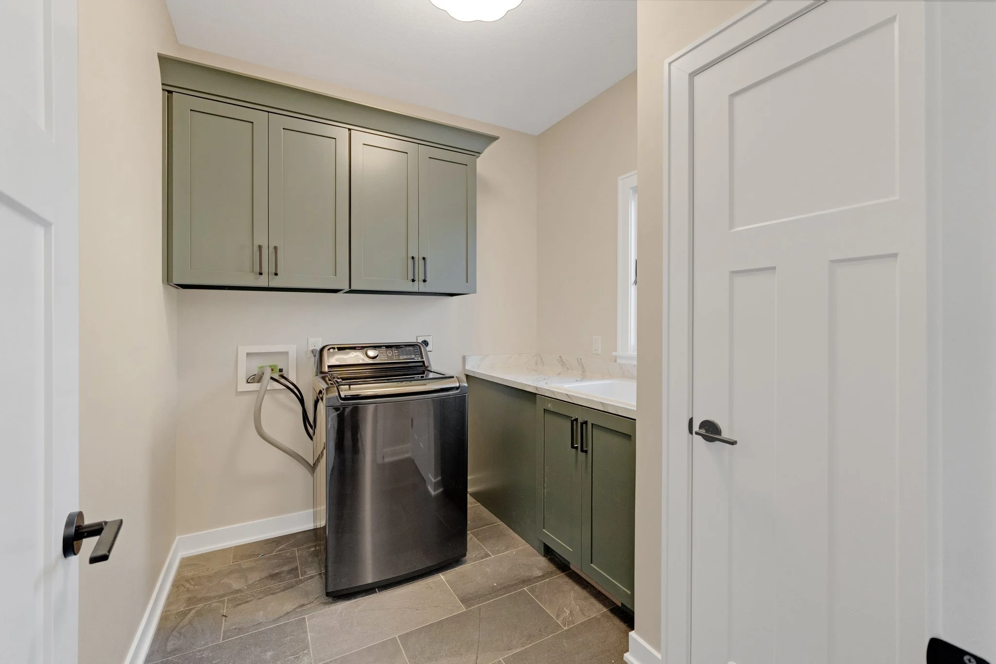 Laundry room with green cabinets, a washing machine, beige walls, and a window.