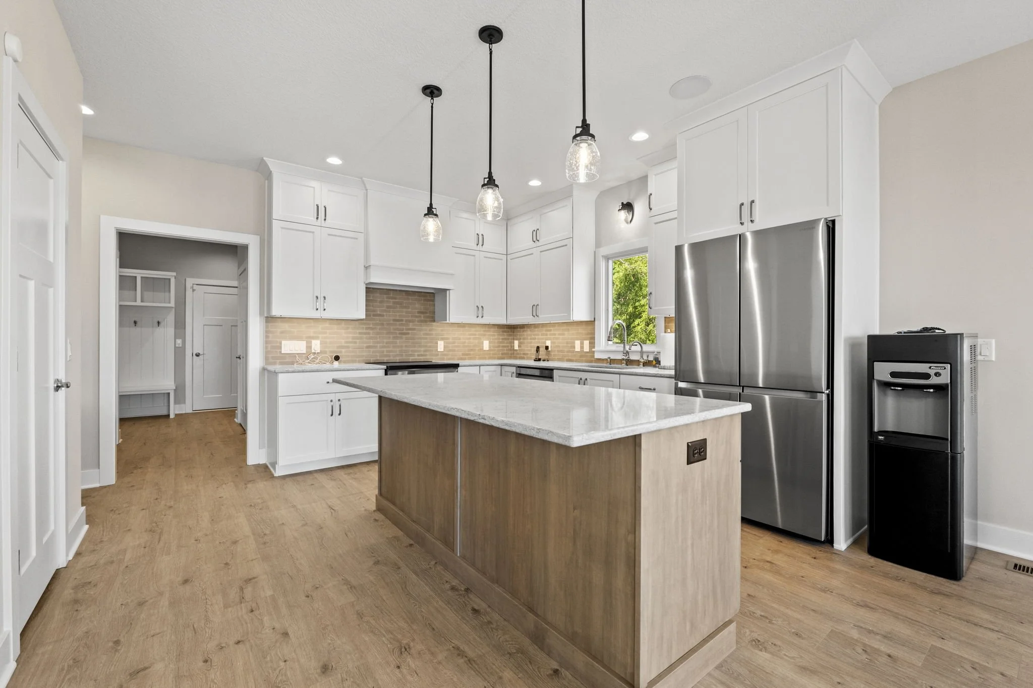 Modern kitchen with white cabinets, stainless steel appliances, a central island with a marble top, pendant lights, and hardwood flooring.