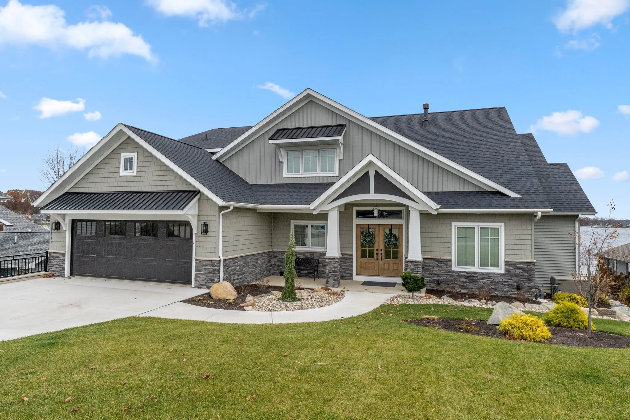 Front view of a modern house with gray siding, stone accents, a landscaped yard, and a double garage