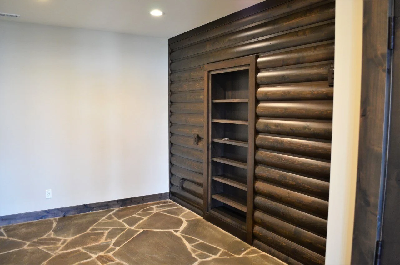 Corner of a room with a dark wooden log-style accented wall, a built-in open shelving unit, and a stone floor.