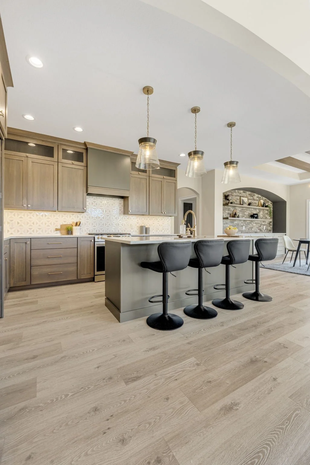 Modern kitchen with wooden cabinets, a large island with four black bar stools, pendant lights, and a light wood floor.