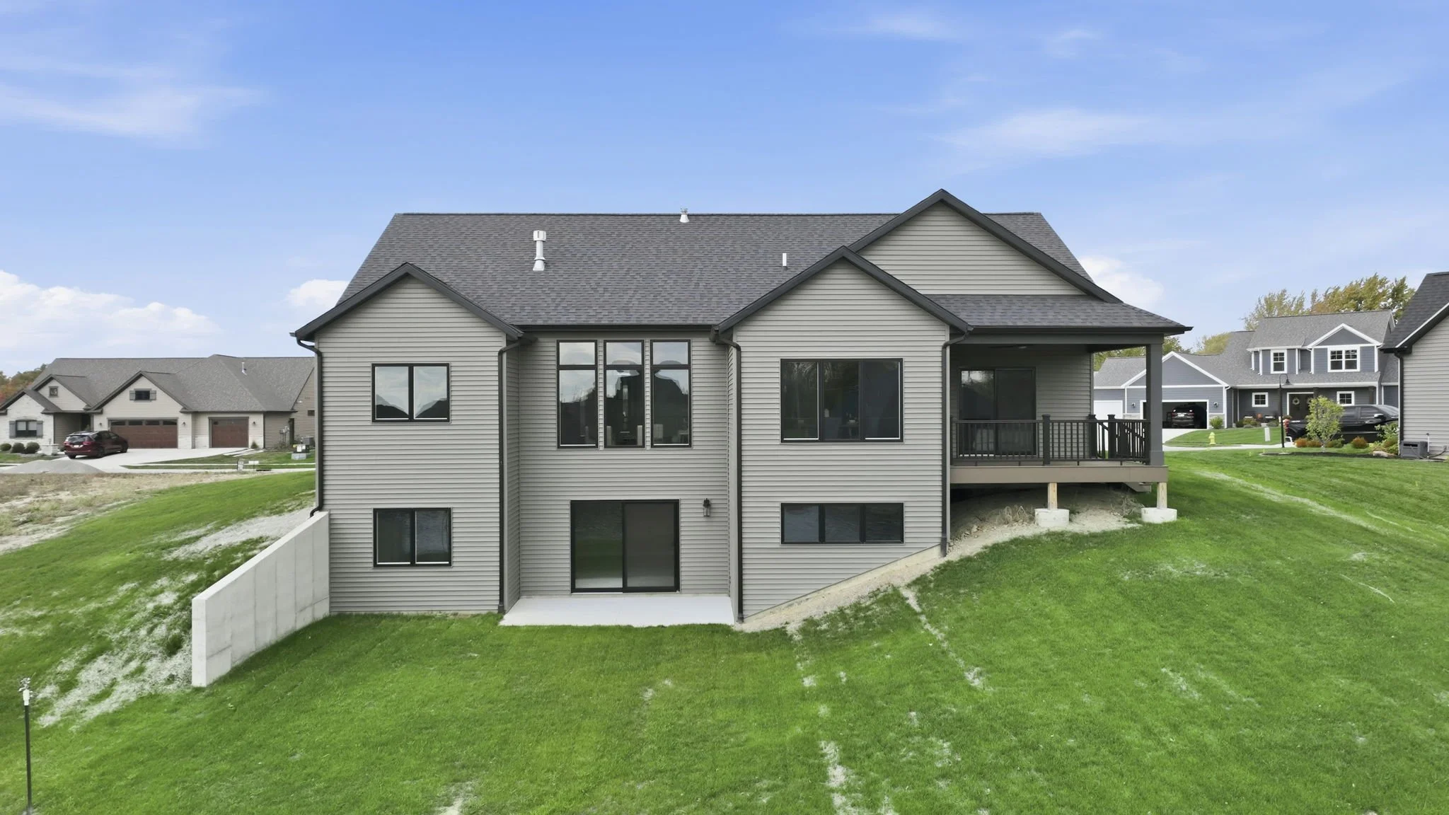 Front view of a two-story house with siding, large windows, a deck on the right side, and a sloped grassy yard.