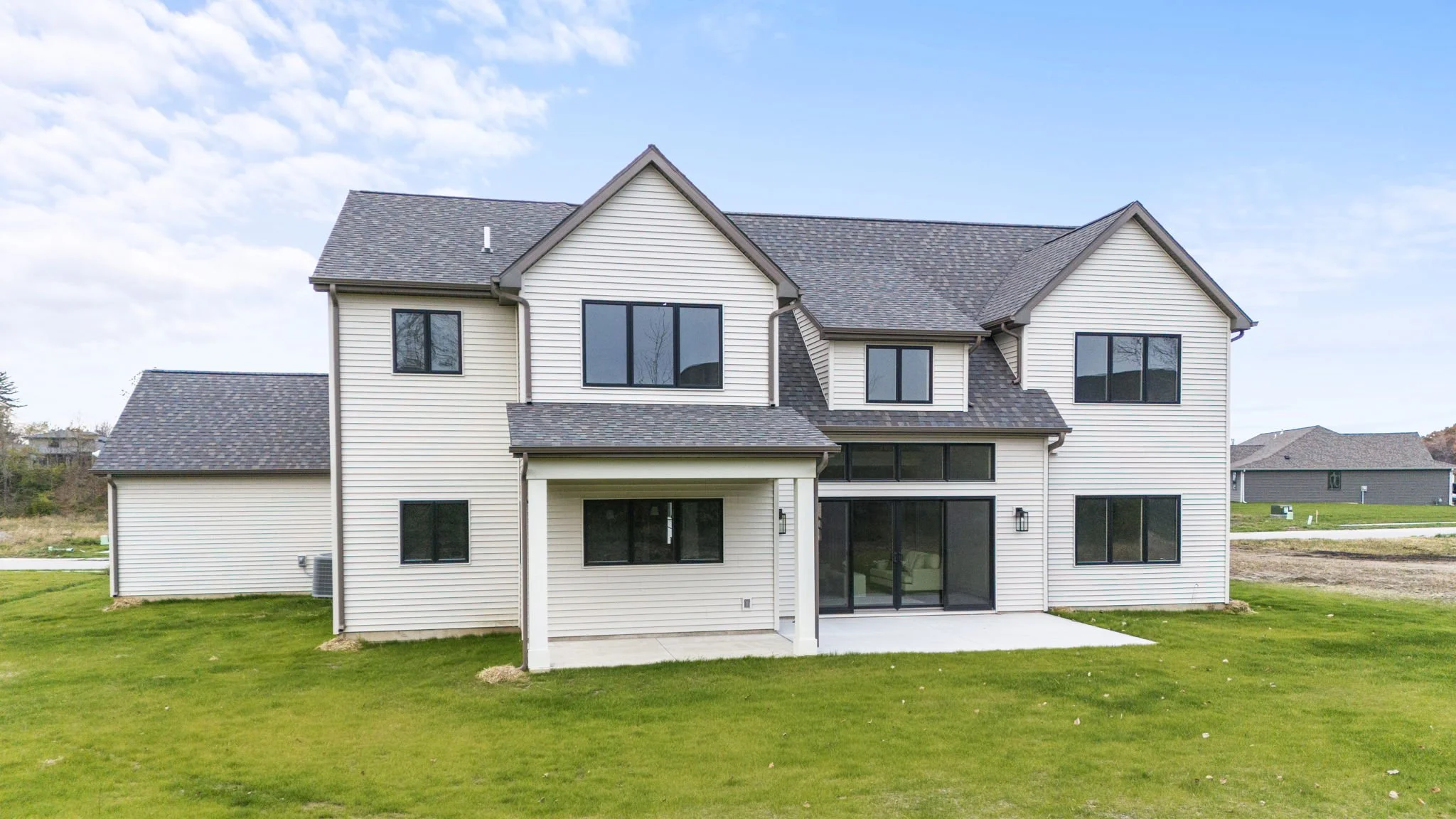 Newly built two-story house with white siding and dark roof, large windows, and a lawn in the backyard.