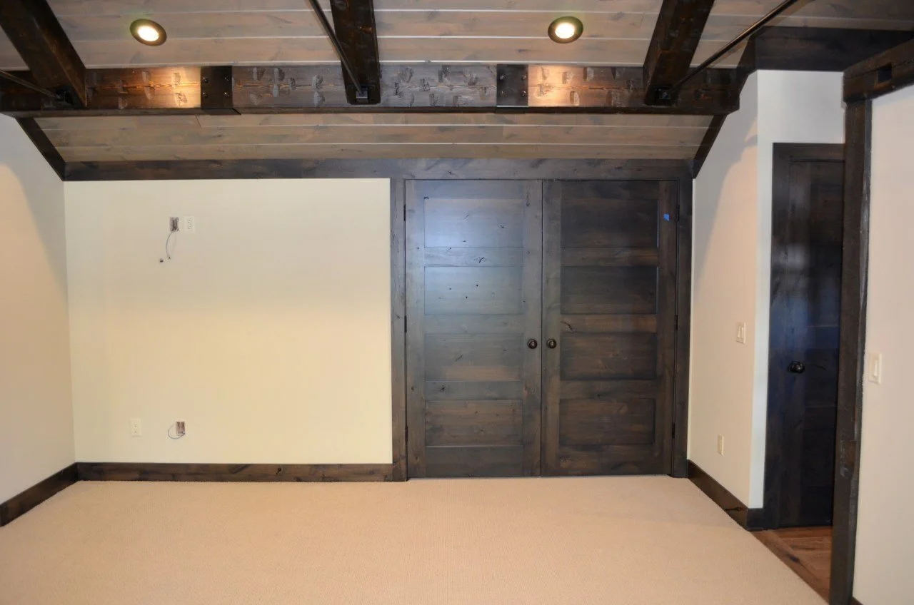 Empty room with beige carpet, white walls, dark wood trim, and sliding dark wood doors.