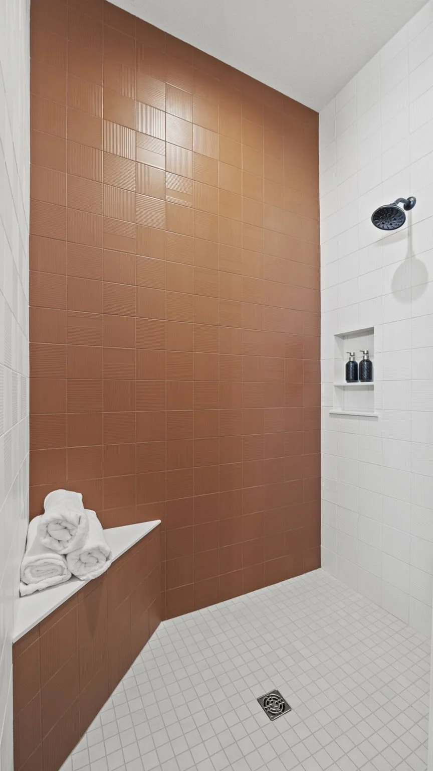 Modern shower with white and terracotta tiles, a showerhead, a niche with soap dispensers, and towels on a built-in bench.