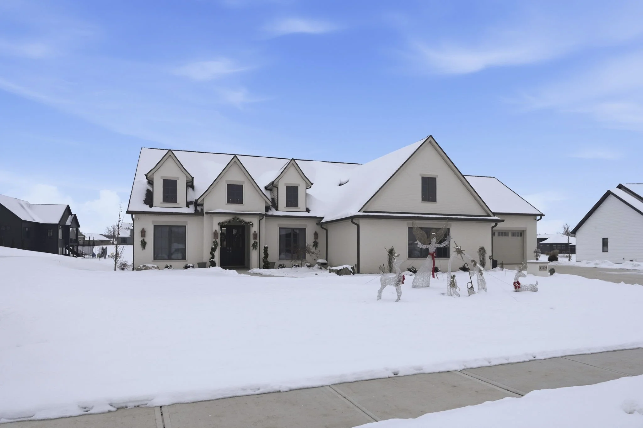 A white house with multiple gables, decorated with holiday decorations, and surrounded by snow. Christmas decorations include illuminated reindeer and other figures in front of the house.