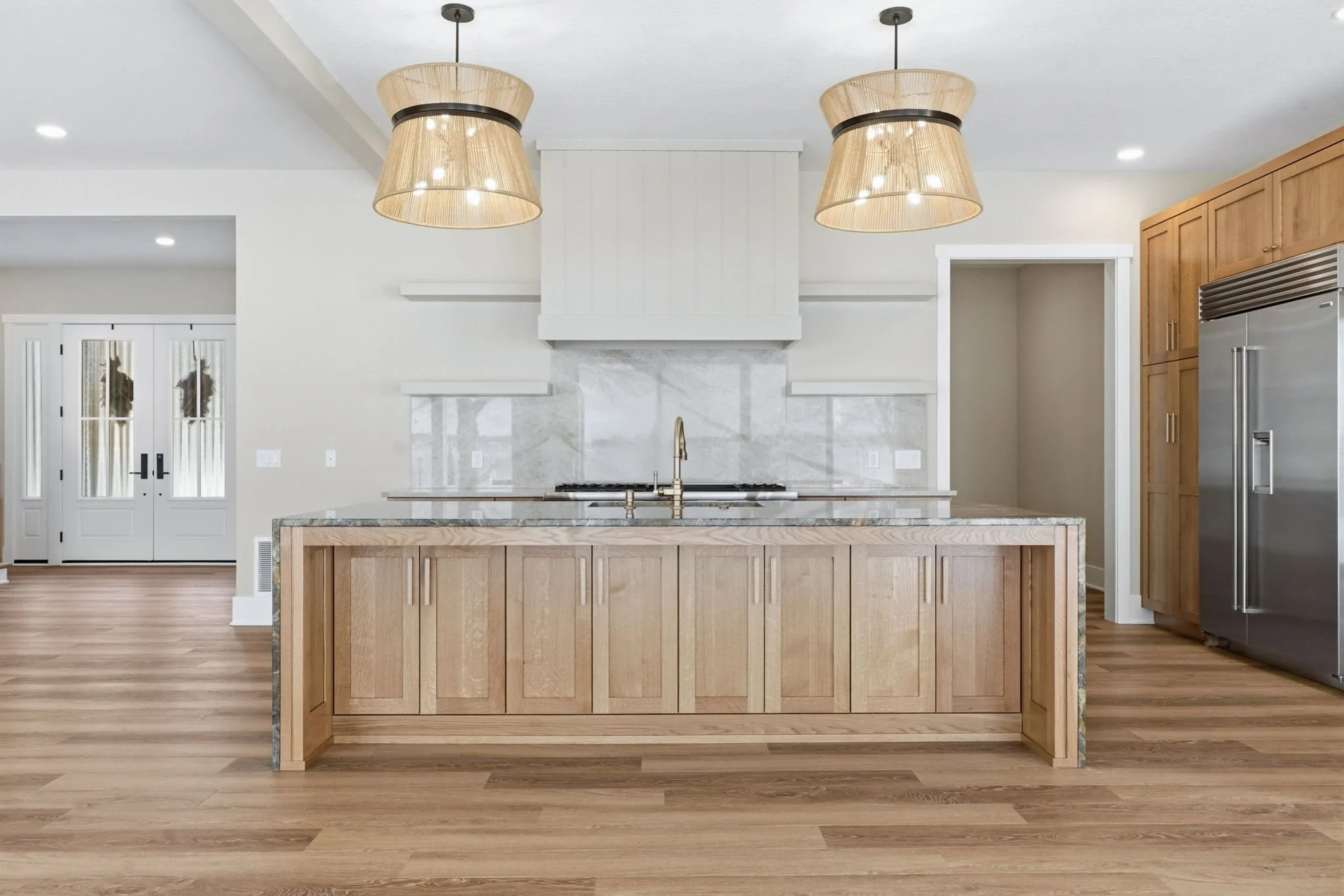 Modern kitchen with wooden island, marble backsplash, stainless steel appliances, and hanging light fixtures.