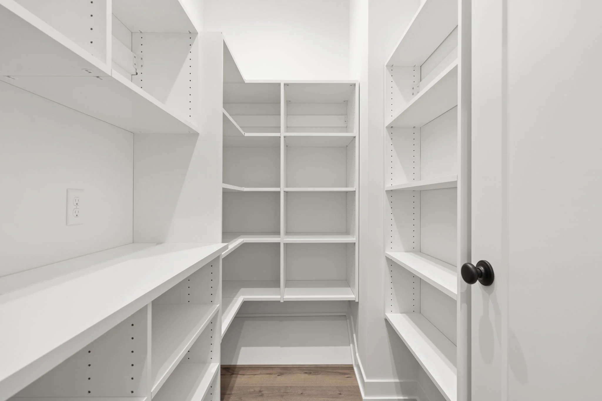 Empty white built-in pantry shelves with a door and wood flooring.