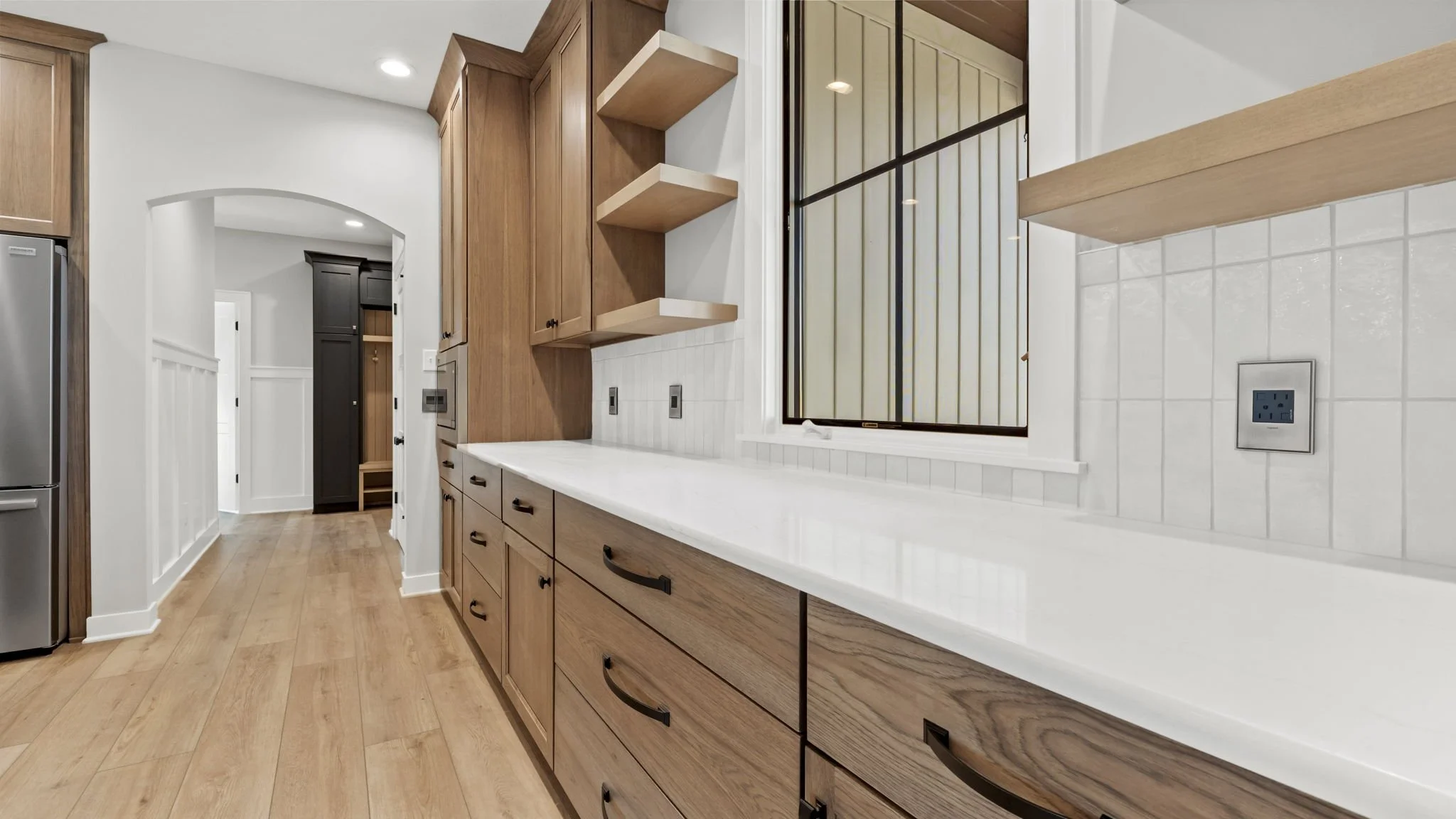 Kitchen with wooden cabinets, white countertop, white tiled backsplash, and a window with black framing.