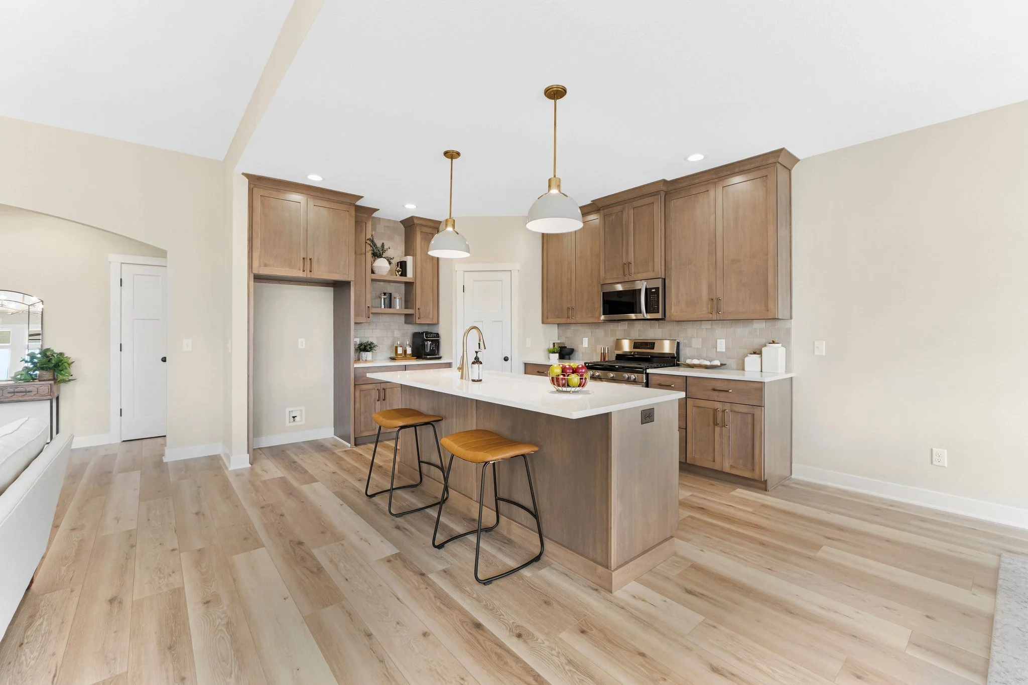 Modern kitchen with wooden cabinets, white countertops, a kitchen island with two yellow bar stools, and stainless steel appliances.