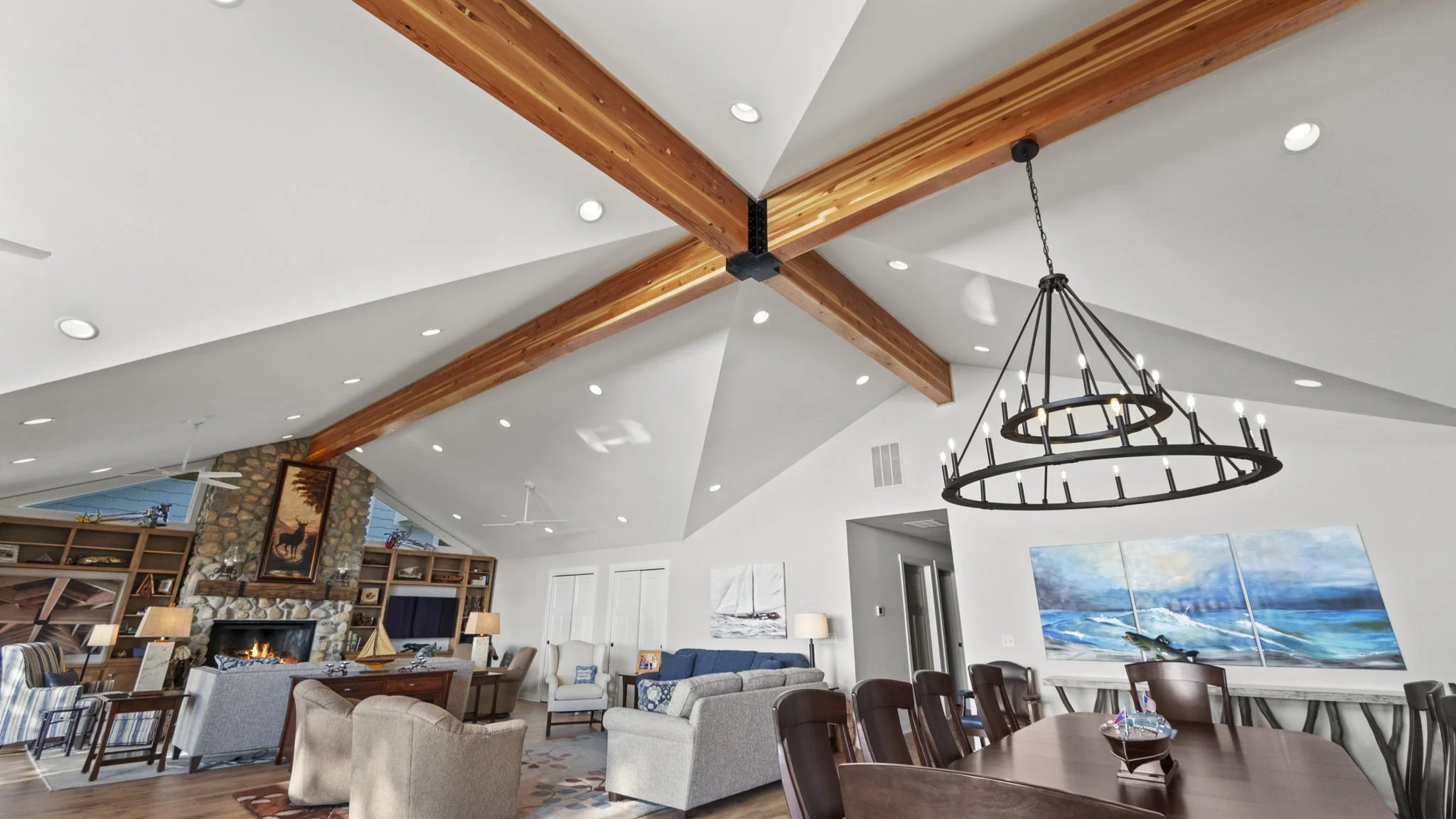 Living room with a vaulted ceiling, exposed wood beams, a chandelier, and a stone fireplace with a painting of a moose above it.