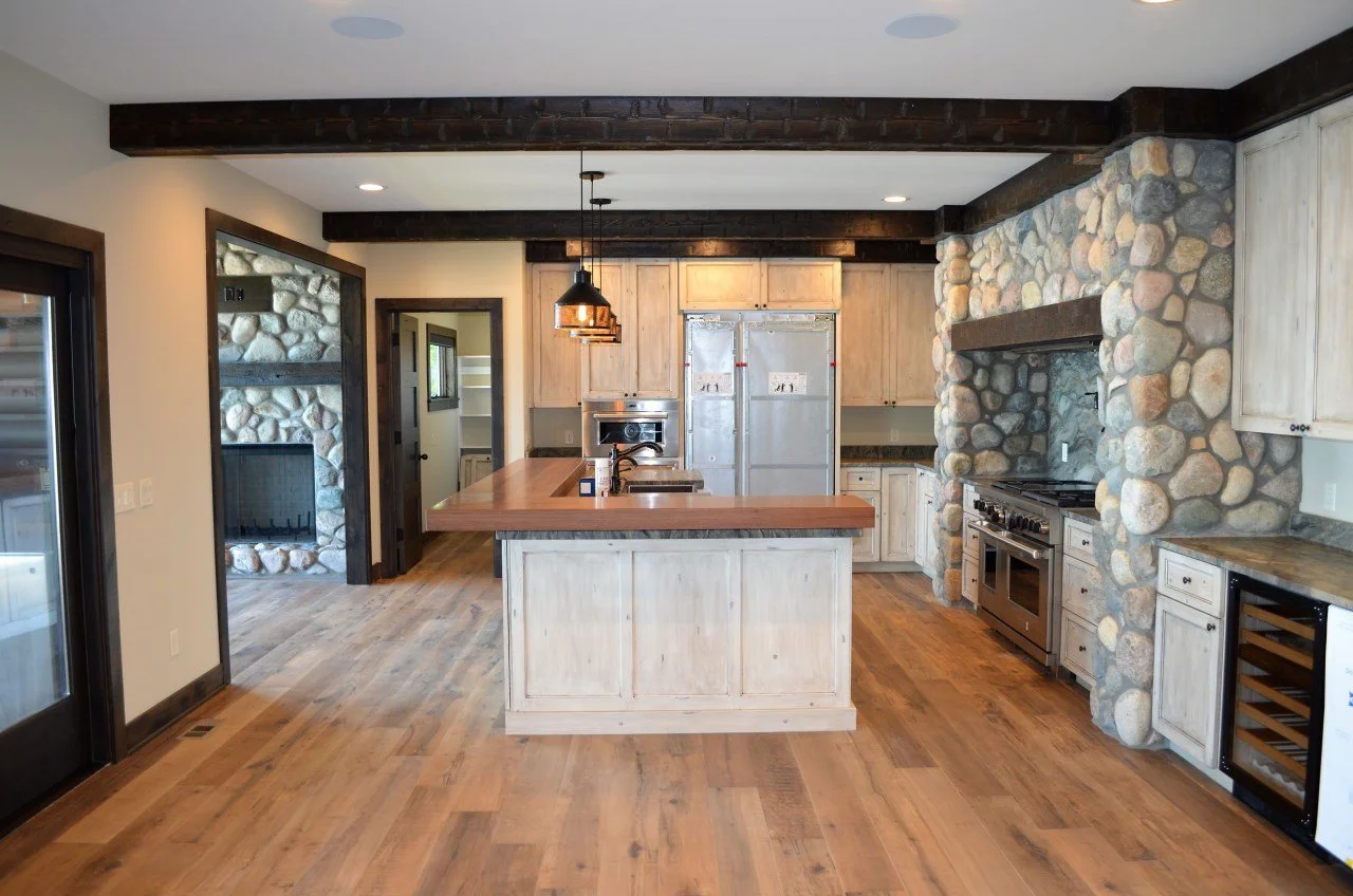 Kitchen with central island, stone wall around fireplace, wooden cabinets, and hardwood floors.