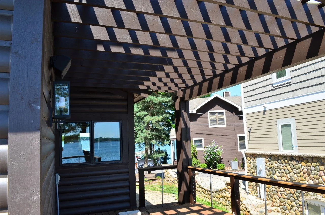 View from a porch overlooking neighboring houses with a lake visible in the distance; the porch is shaded by a lattice overhead.