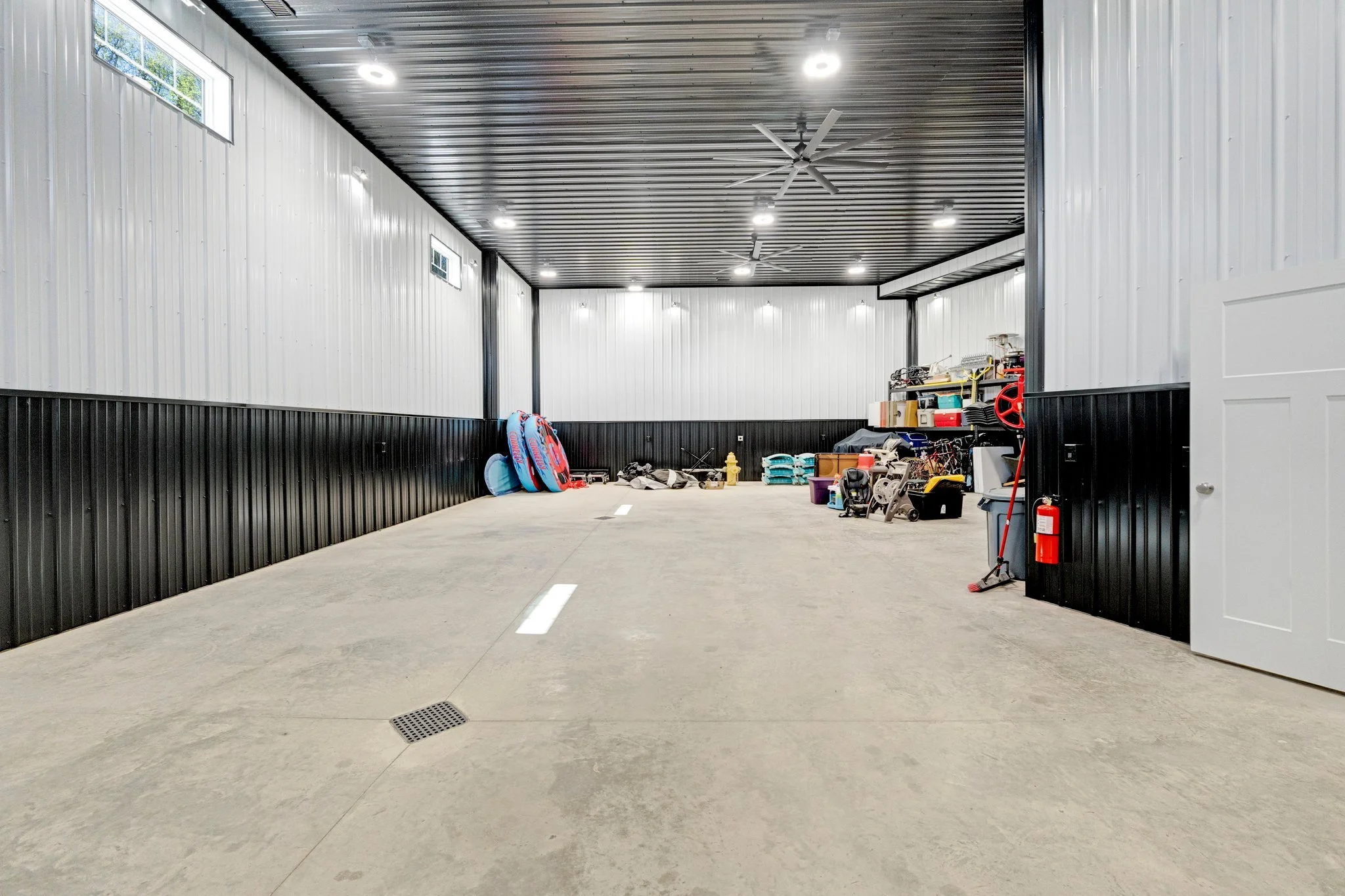 Empty garage with cleaning tools, stacked pool floats, and storage shelves along the back wall.