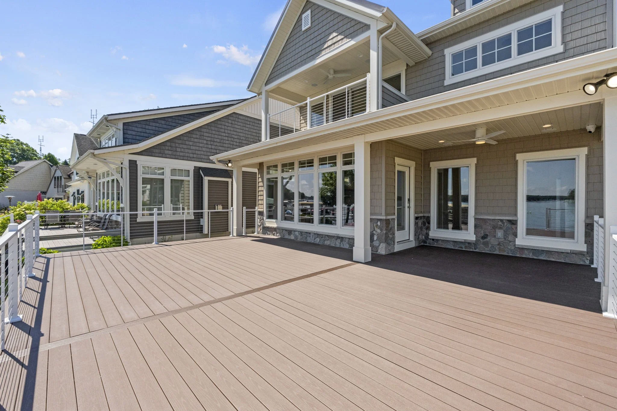 Large outdoor deck area attached to a modern house with multiple windows, a balcony, and exterior lighting.