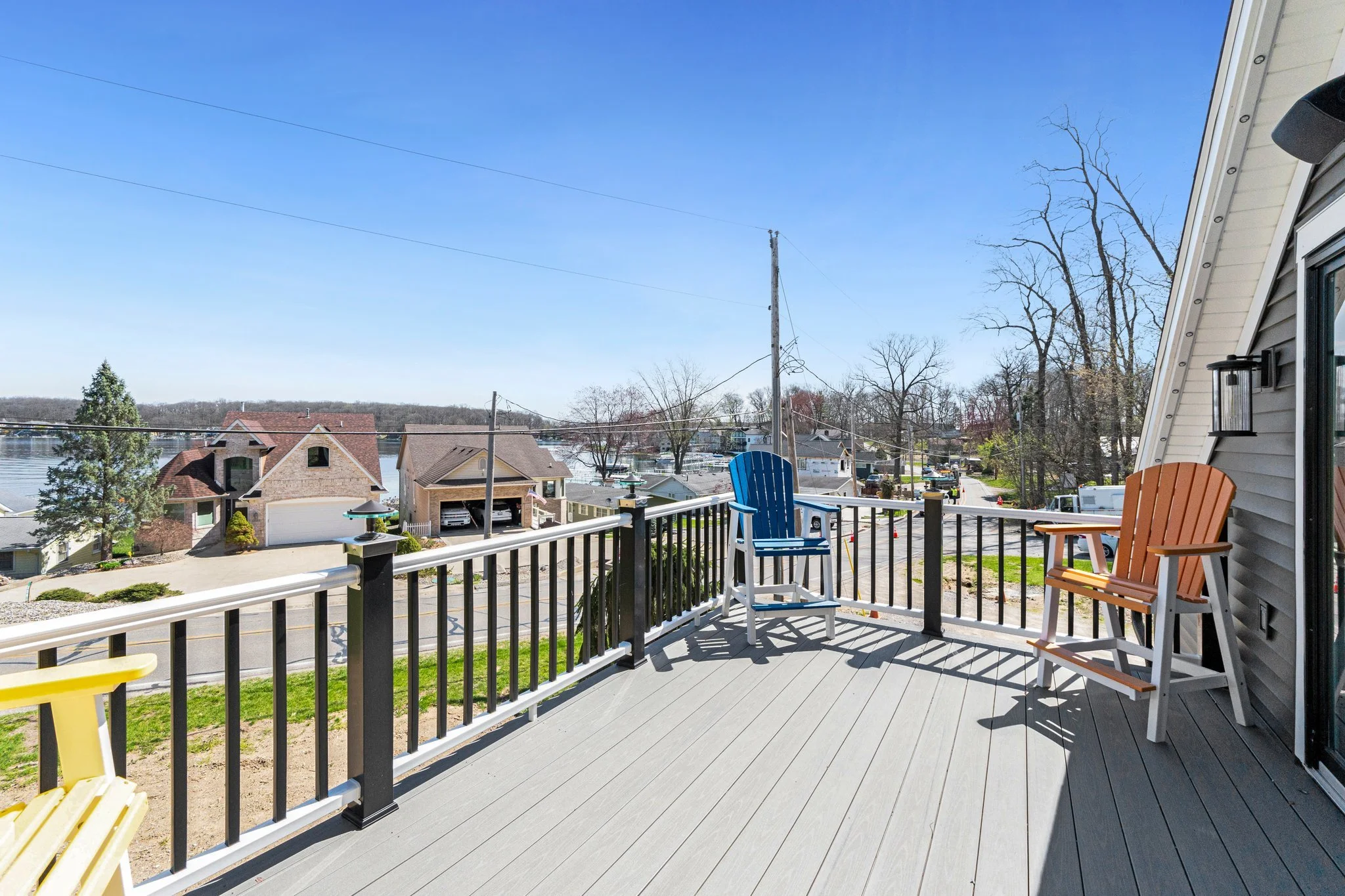 View from a balcony overlooking a neighborhood with houses, trees, and a river under a clear blue sky.